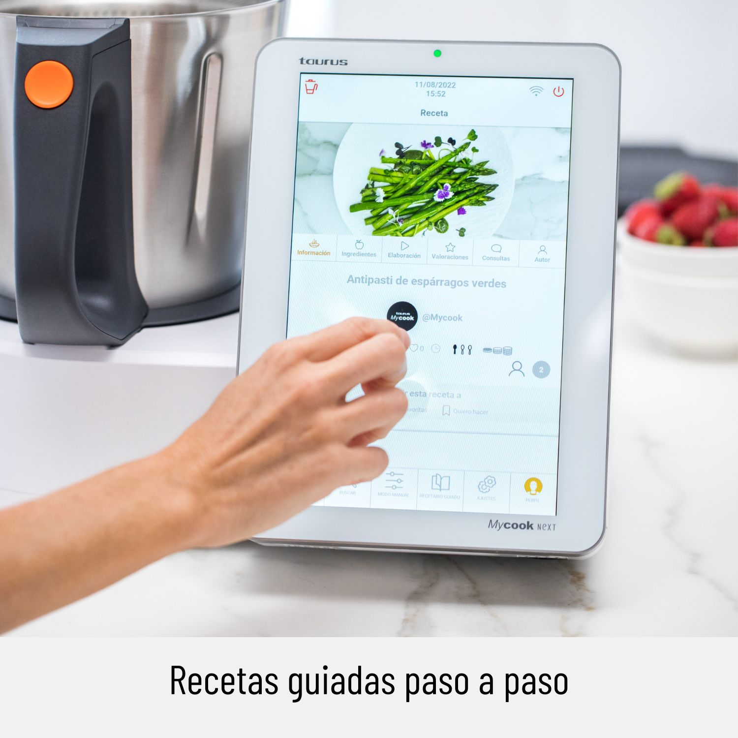 Una mano usando una tableta que muestra una receta con espárragos verdes en un plato, con otros ingredientes.