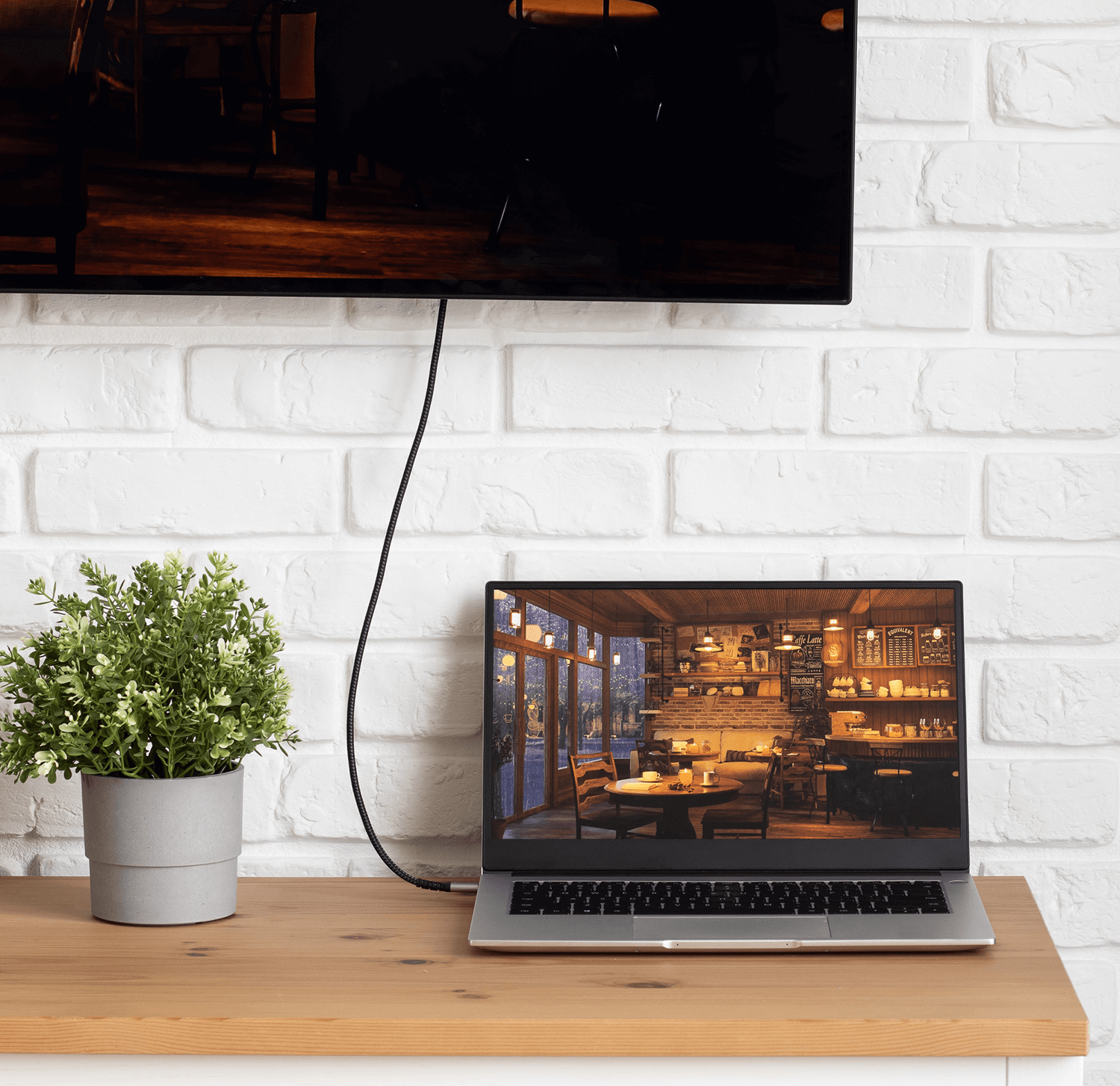 Laptop podłączony do telewizora na drewnianym stole, z rośliną w pobliżu.