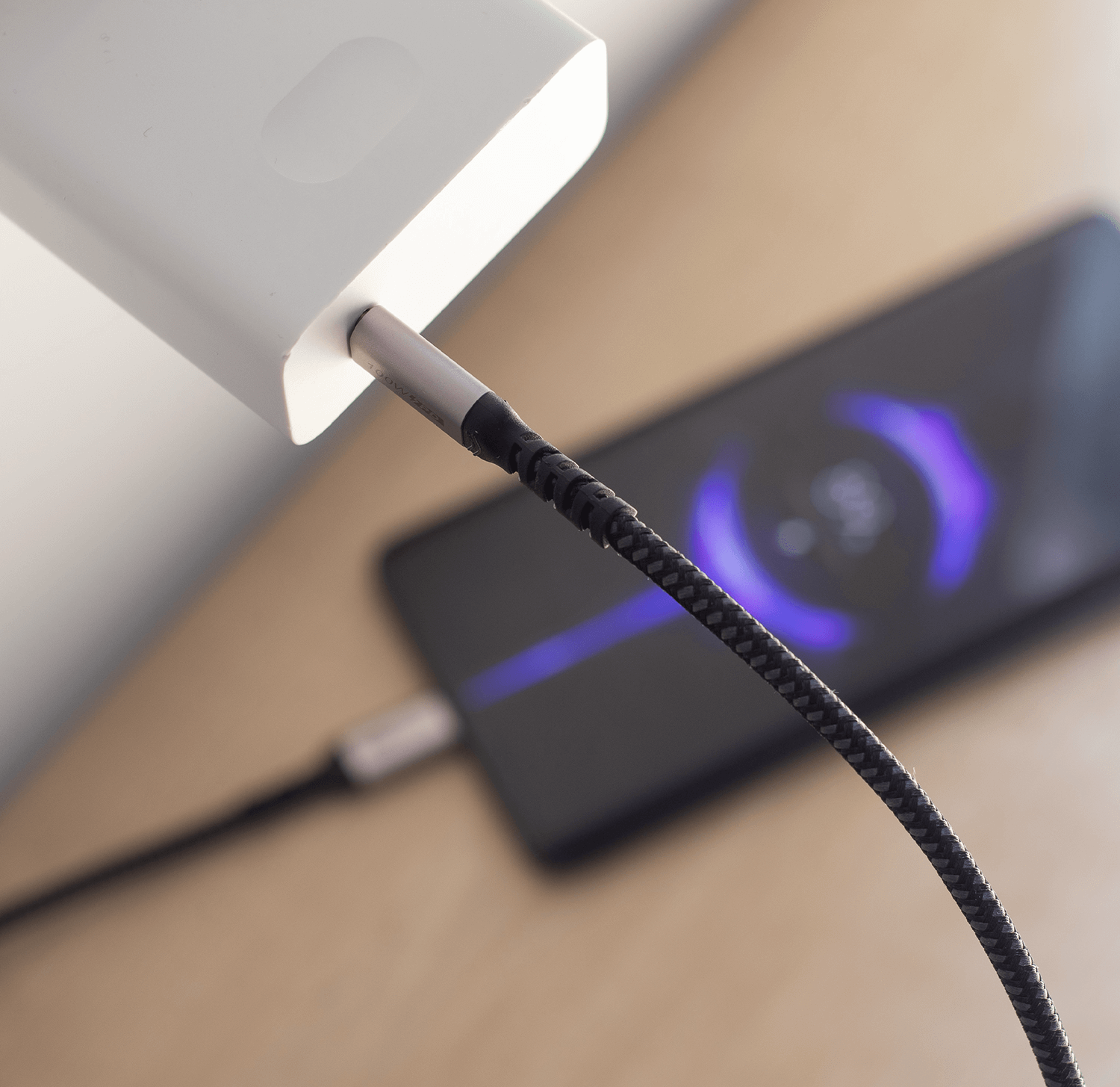 Telefon ładuje się na stole. Kabel jest podłączony do telefonu i zasilacza.