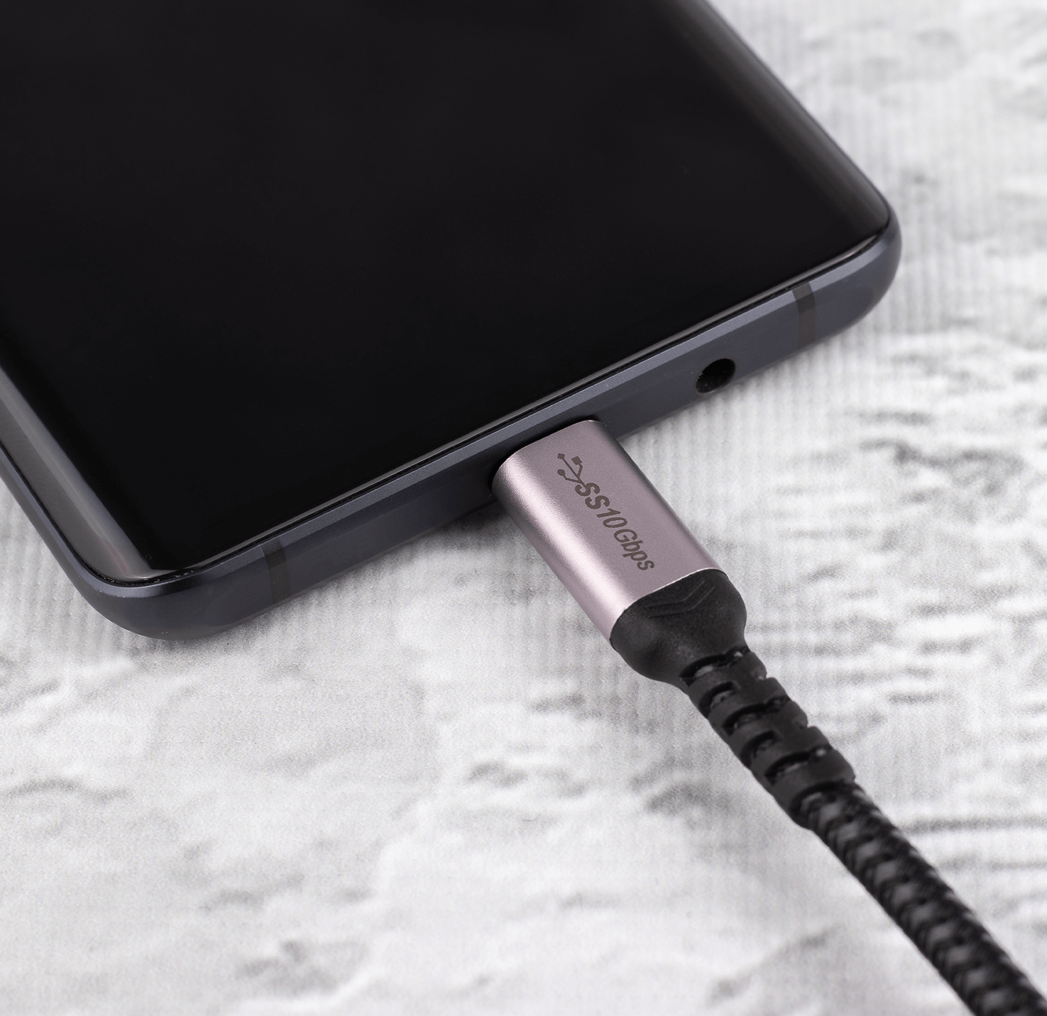 Czarny smartfon podłączony do kabla USB-C. Kabel jest srebrny i czarny.