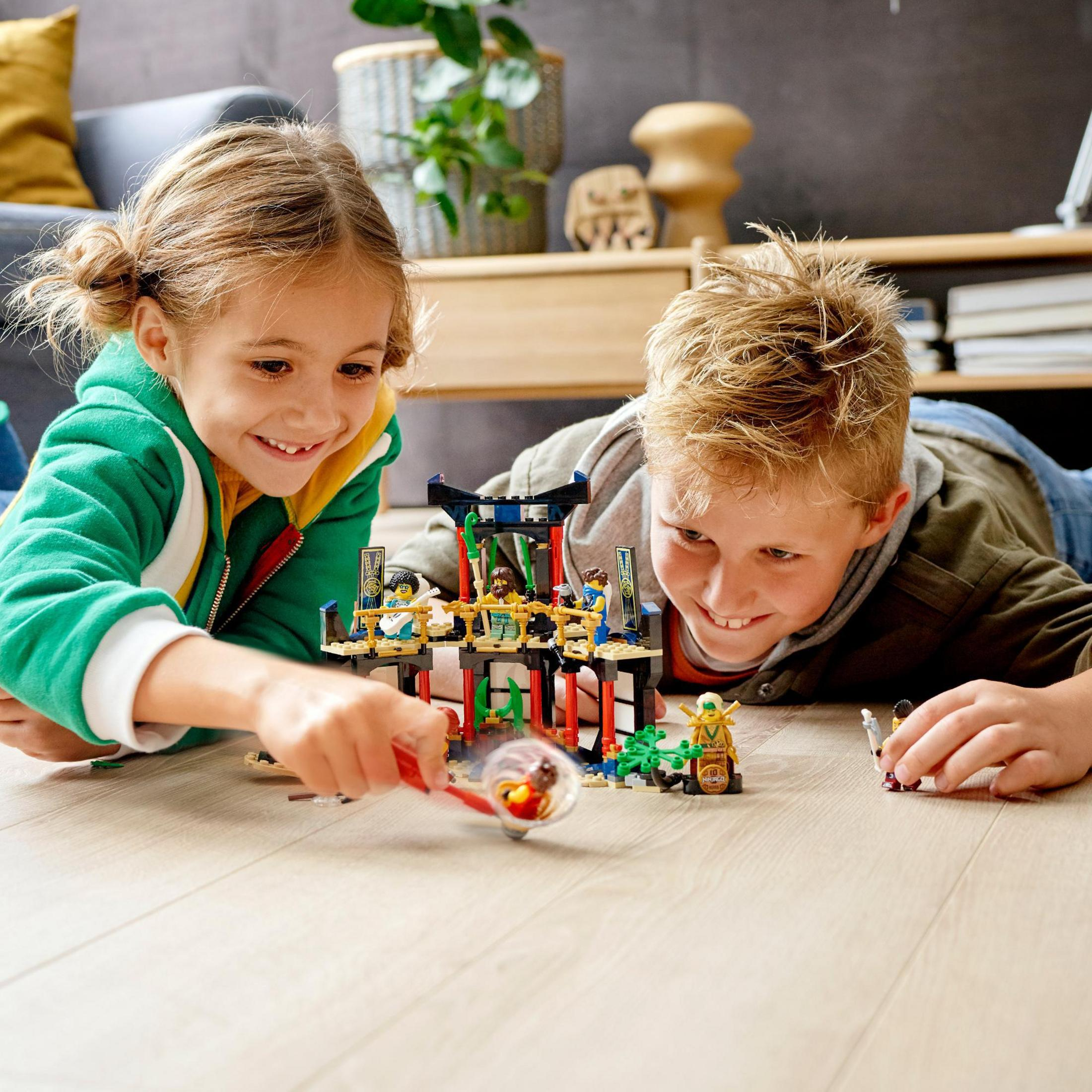 Due bambini giocano con un set Lego sul pavimento, sorridendo e impegnati.