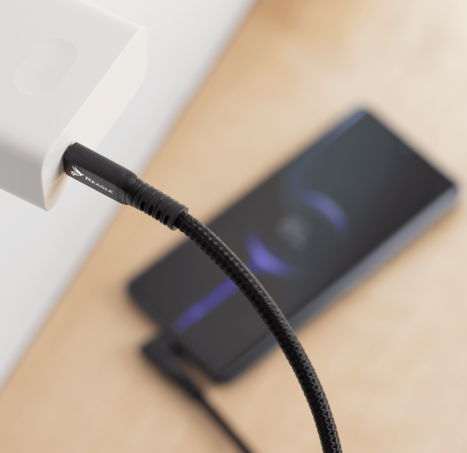 Czarny kabel ładujący podłączony do białej ładowarki. Telefon jest częściowo widoczny w tle, w trakcie ładowania.