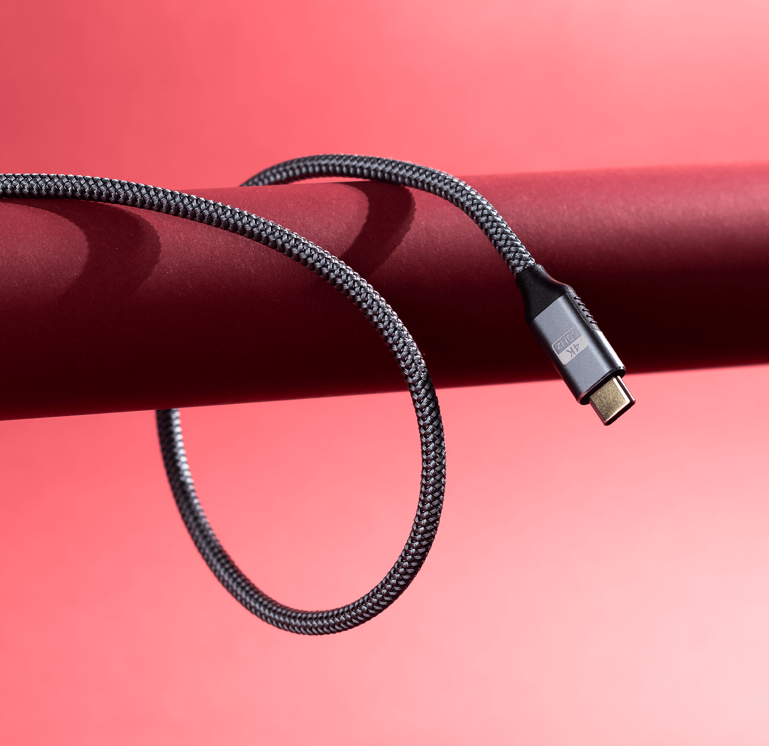 Pleciony kabel USB-C, ciemnoszary, zakrzywiony wokół czerwonego cylindrycznego obiektu.