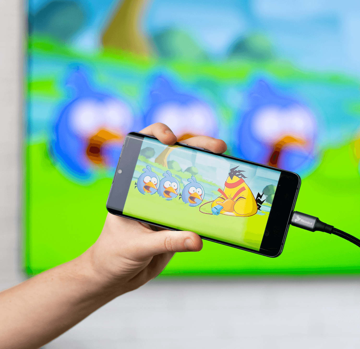 Osoba trzyma telefon z grą Angry Birds na ekranie telewizora. Ekran wyświetla ptaki i żółtego ptaka.