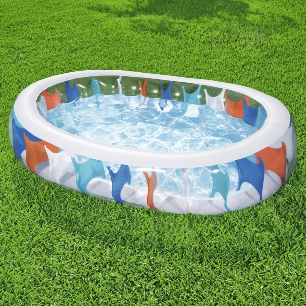 Piscine gonflable de forme ovale remplie d'eau. Elle est placée sur de l'herbe verte. La piscine présente des motifs colorés sur le côté.