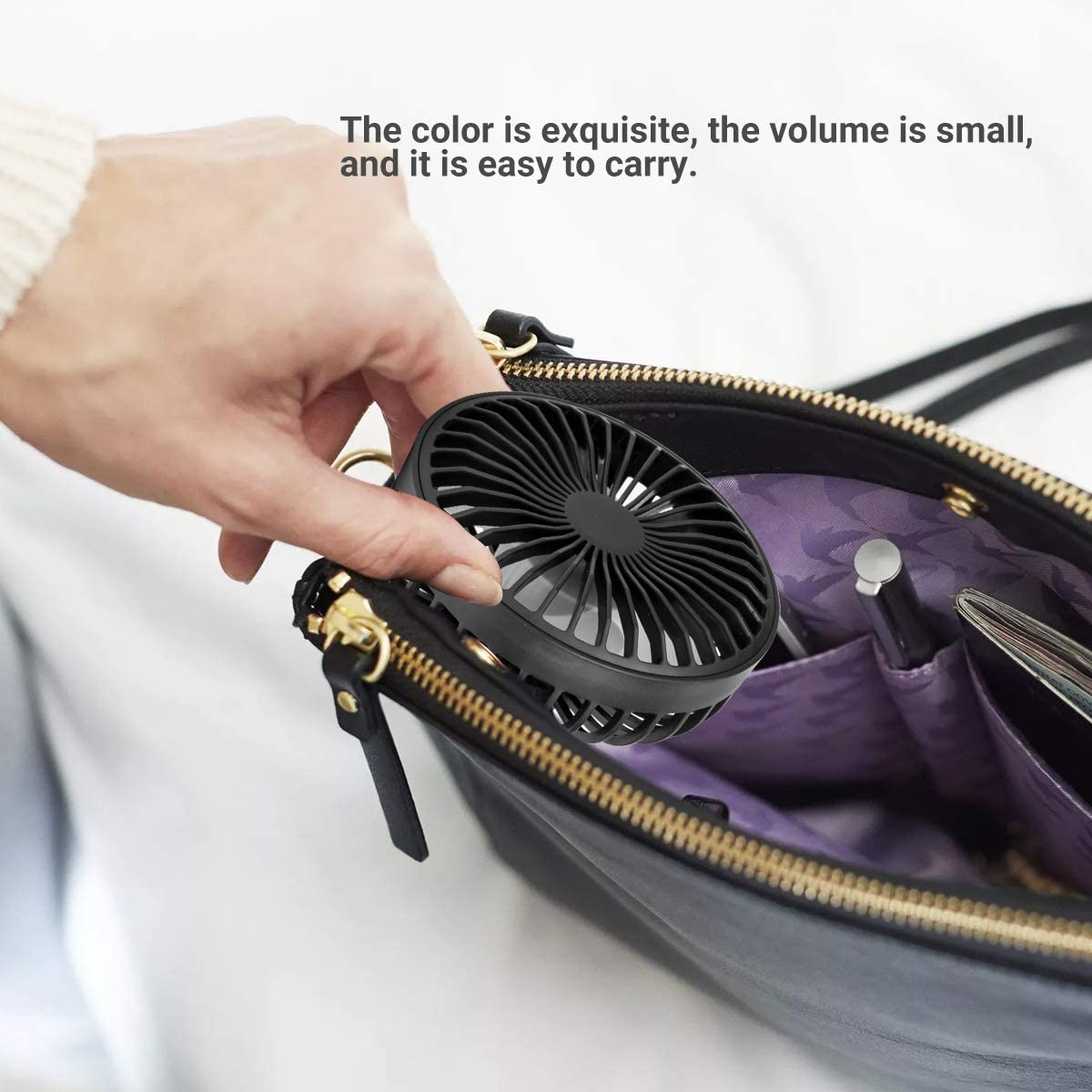 Eine Hand hält einen schwarzen Mini-Ventilator aus einer schwarzen Tasche. Der Ventilator hat ein kreisförmiges Design.