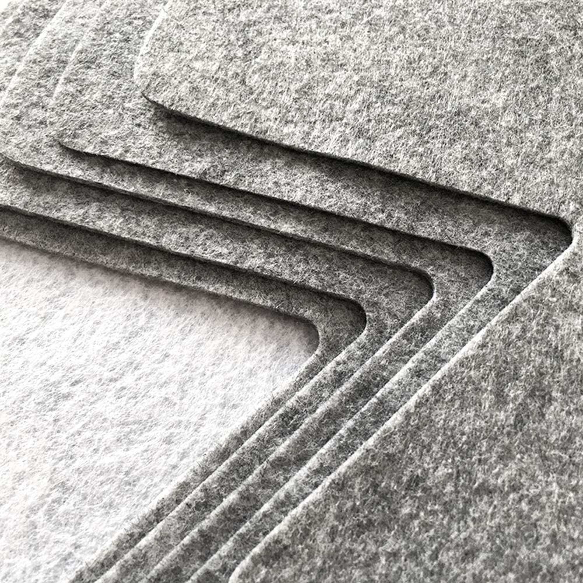 Pila de láminas de fieltro gris. Tienen recortes curvos a lo largo de un borde. Las láminas están en capas.