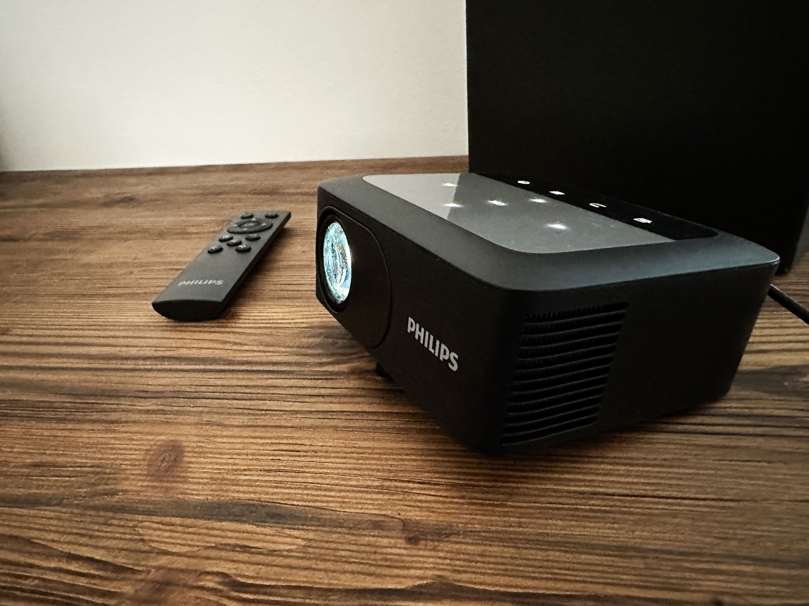 Czarny projektor i pilot na drewnianym stole. Światła włączone.