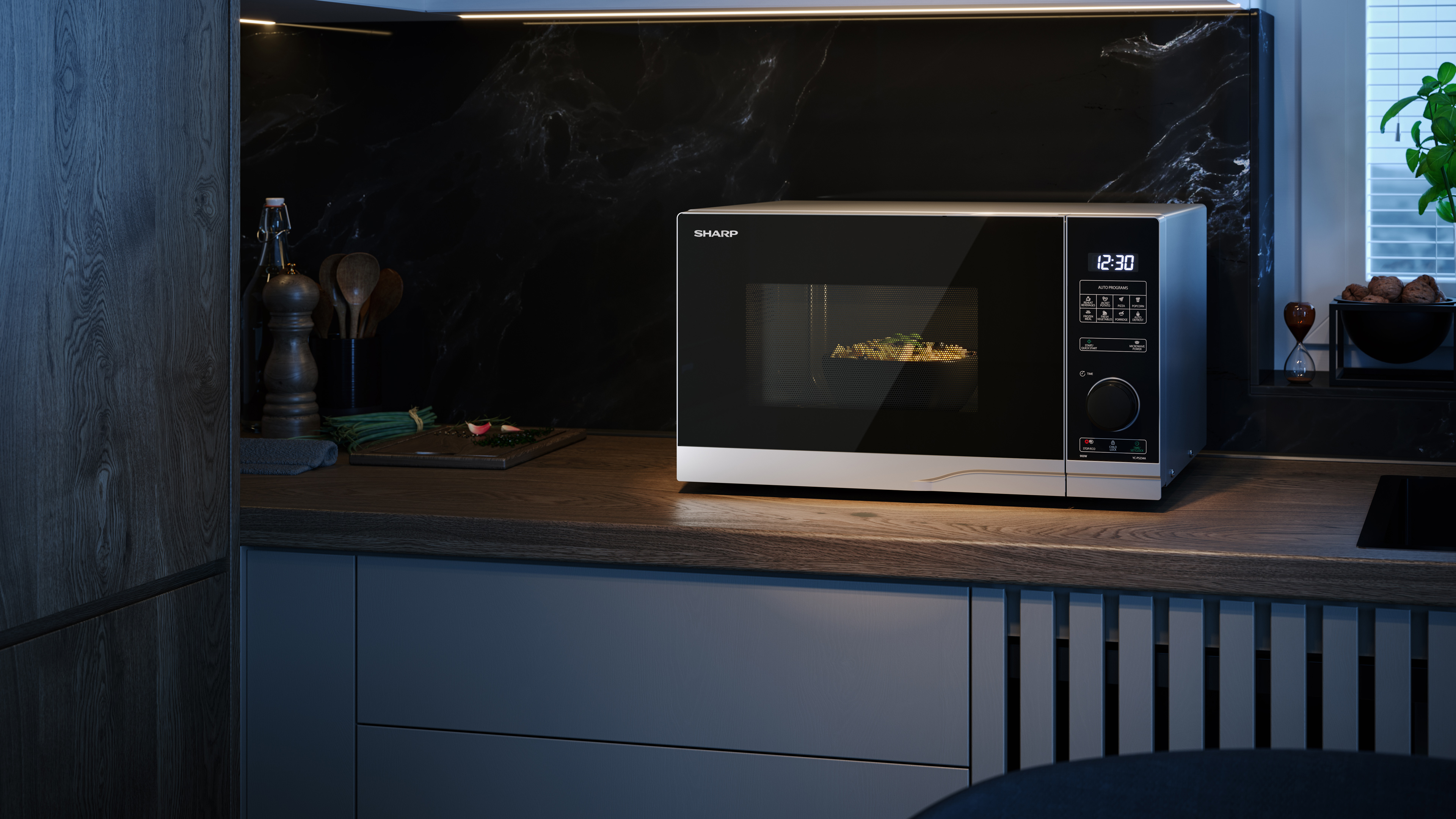 Kuchenka mikrofalowa Sharp na blacie w otoczeniu kuchni. Wyświetlana jest godzina 12:30.