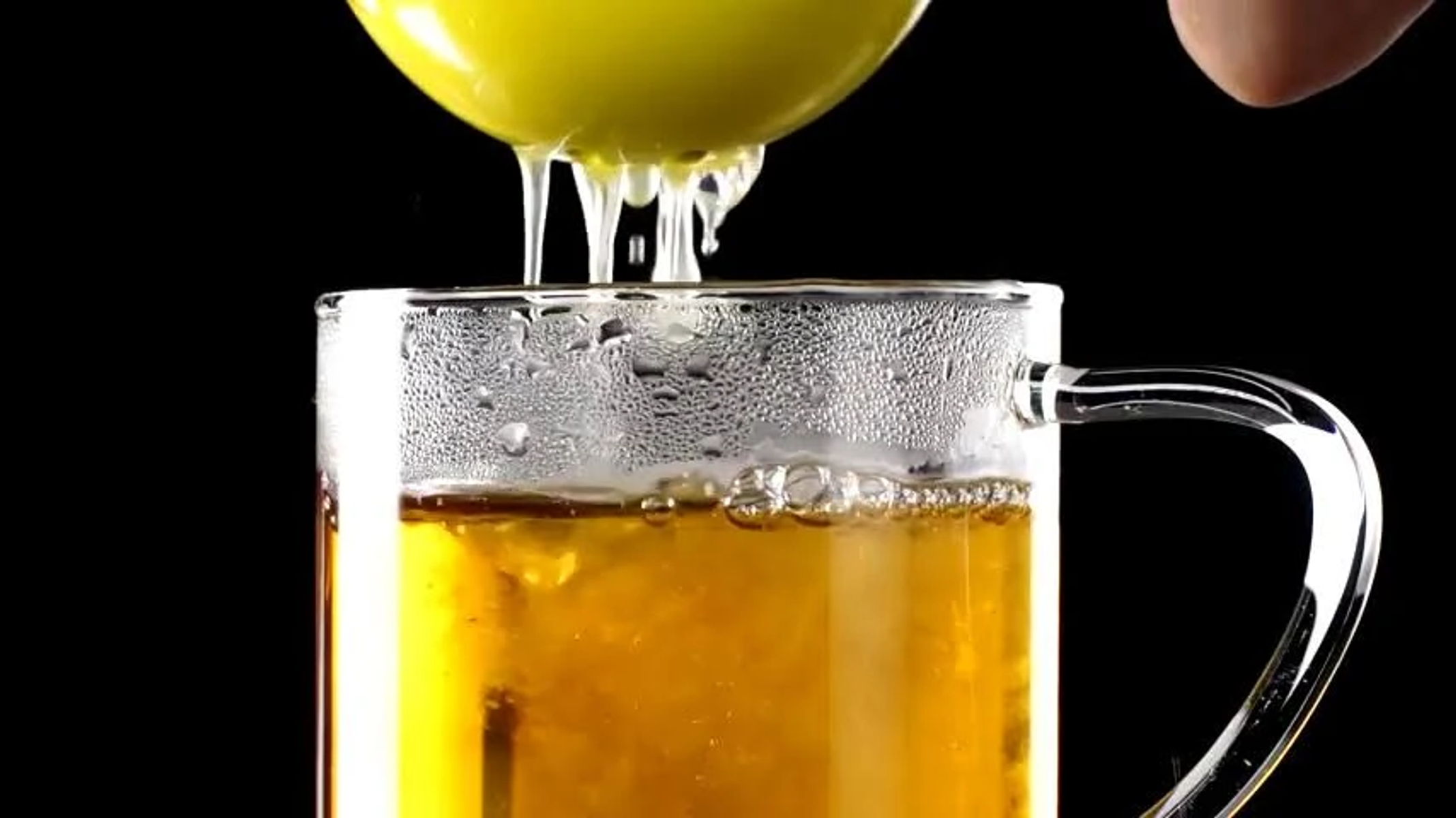 Sok z cytryny wyciskany do szklanego kubka wypełnionego herbatą na czarnym tle.