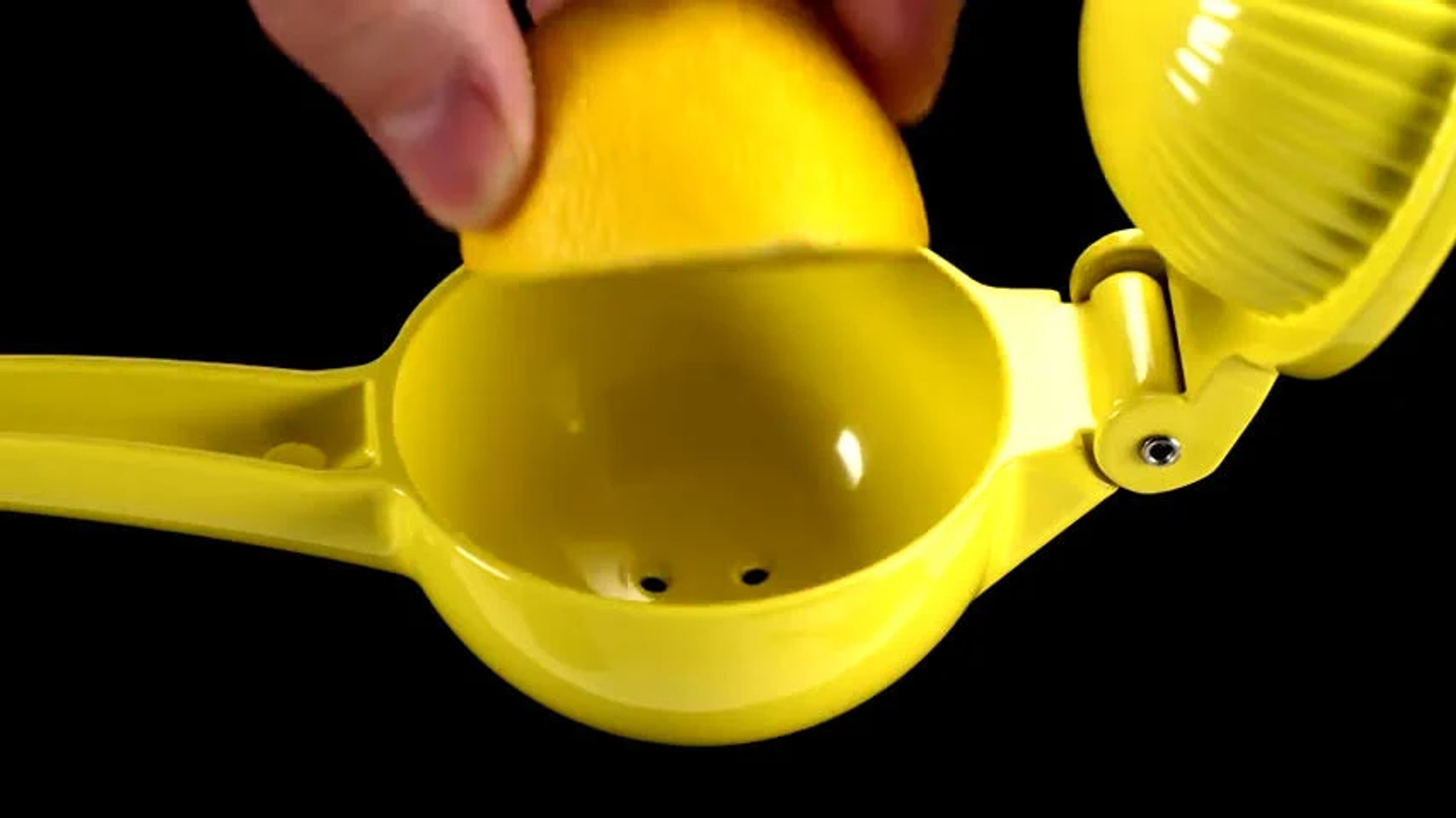 Ręka wyciskająca cytrynę w żółtej wyciskarce do cytrusów na czarnym tle.