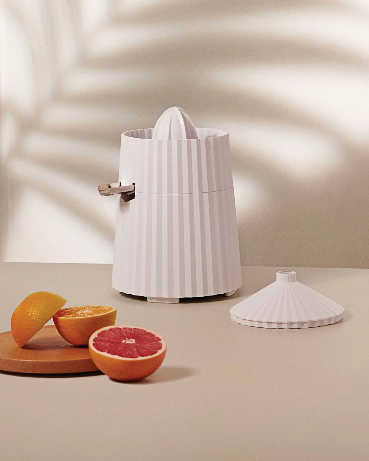 Spremiagrumi bianco a righe verticali, accanto ad arance su un tagliere di legno. Luce naturale.