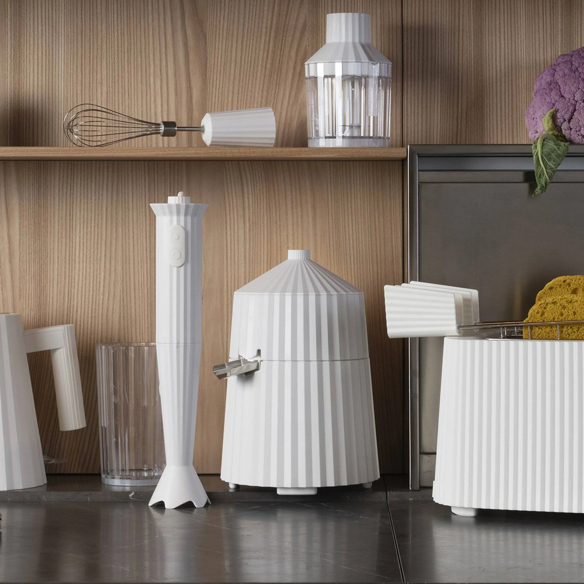 Un piano cucina bianco con elettrodomestici bianchi: frullatore, mixer e altri utensili da cucina su uno scaffale di legno.
