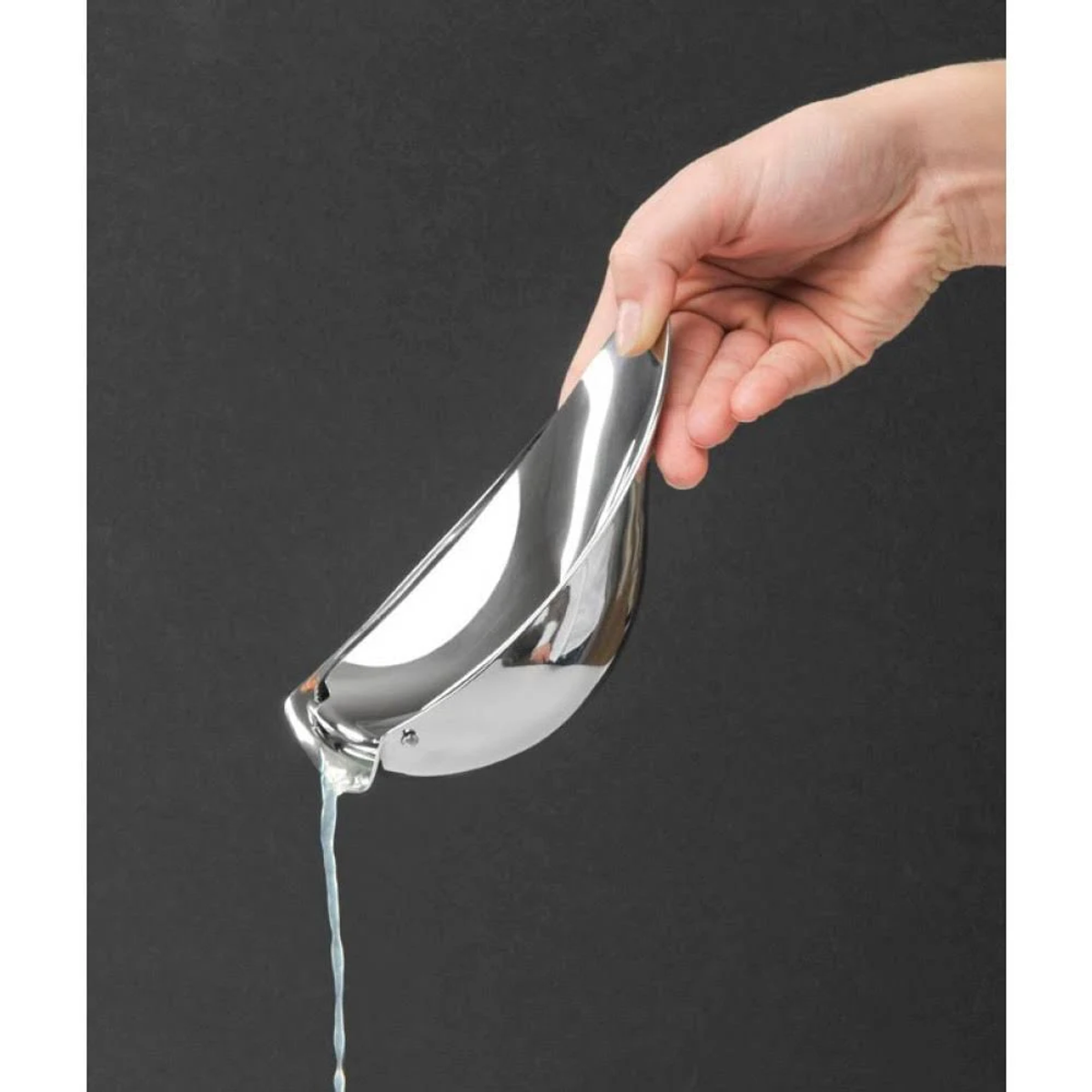 Mano che tiene uno spremiagrumi d'argento, versa succo su sfondo scuro.