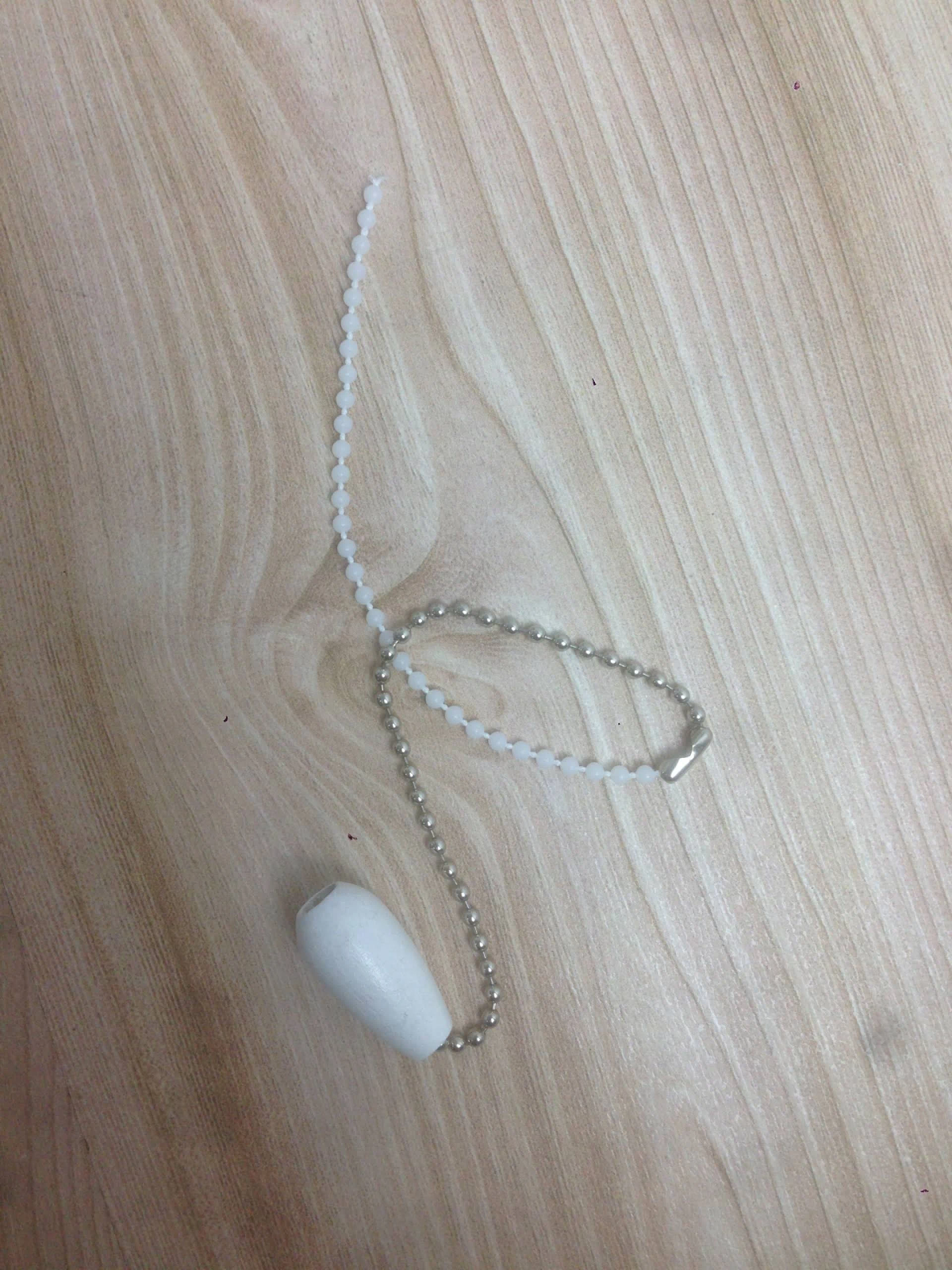 Weiße, perlenbesetzte Zugkordel mit einem weißen, ovalen Griff und einer silbernen Kette. Auf Holzoberfläche.