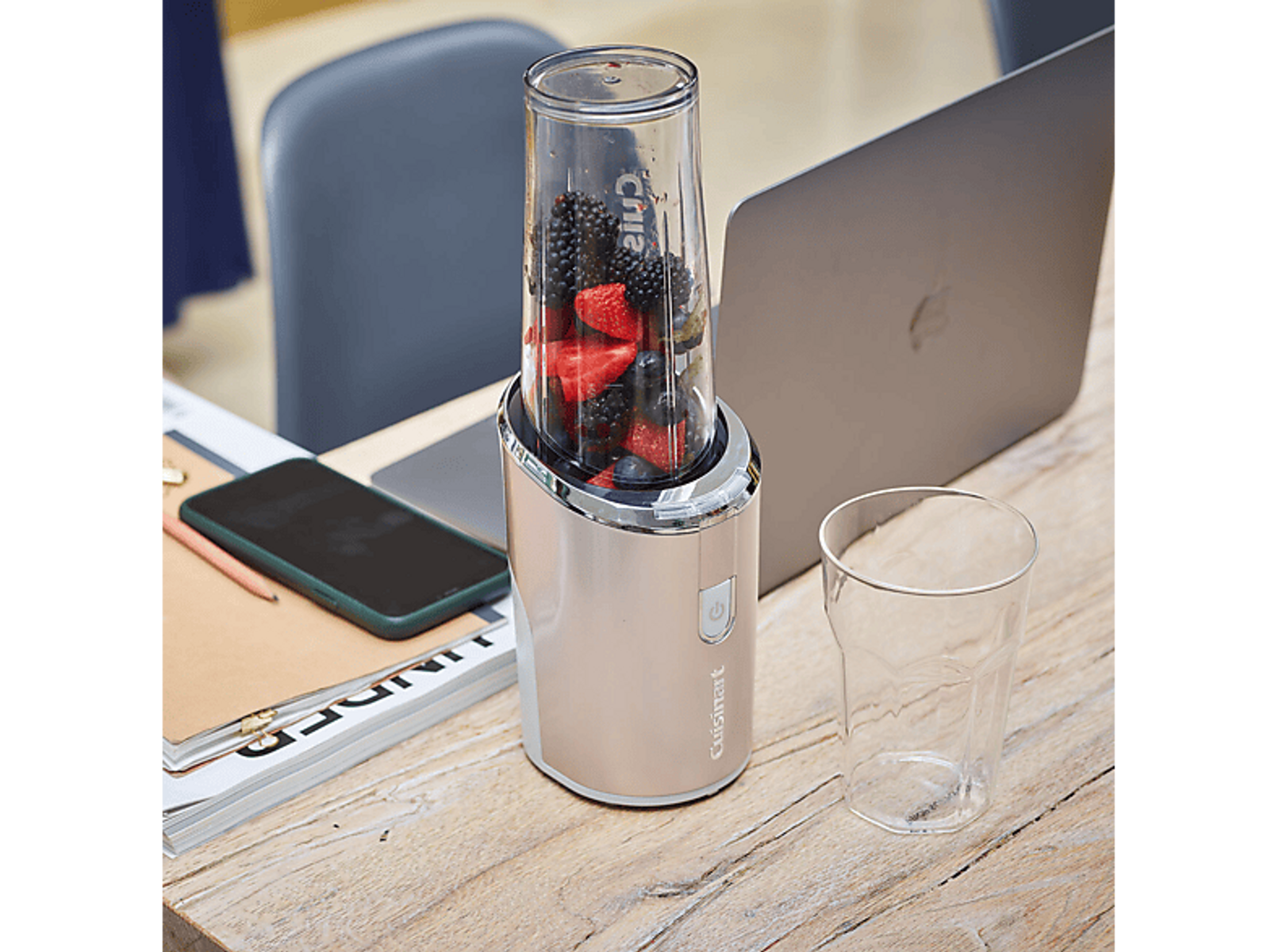 Una licuadora con bayas mixtas. Una laptop, teléfono y vaso sobre un escritorio de madera.