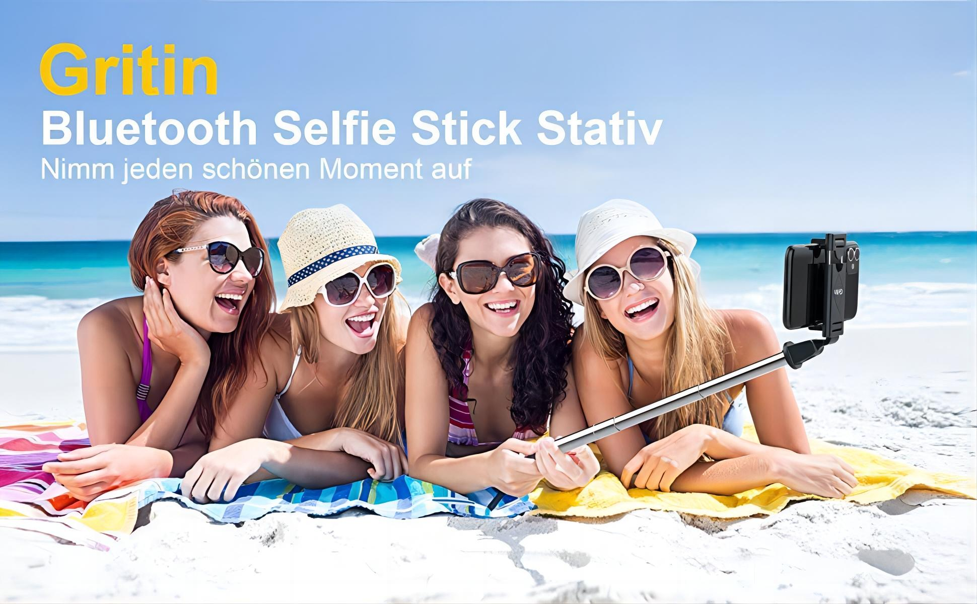 Vier Frauen am Strand, die lächeln und an einem sonnigen Tag ein Selfie mit einem Selfie-Stick machen.