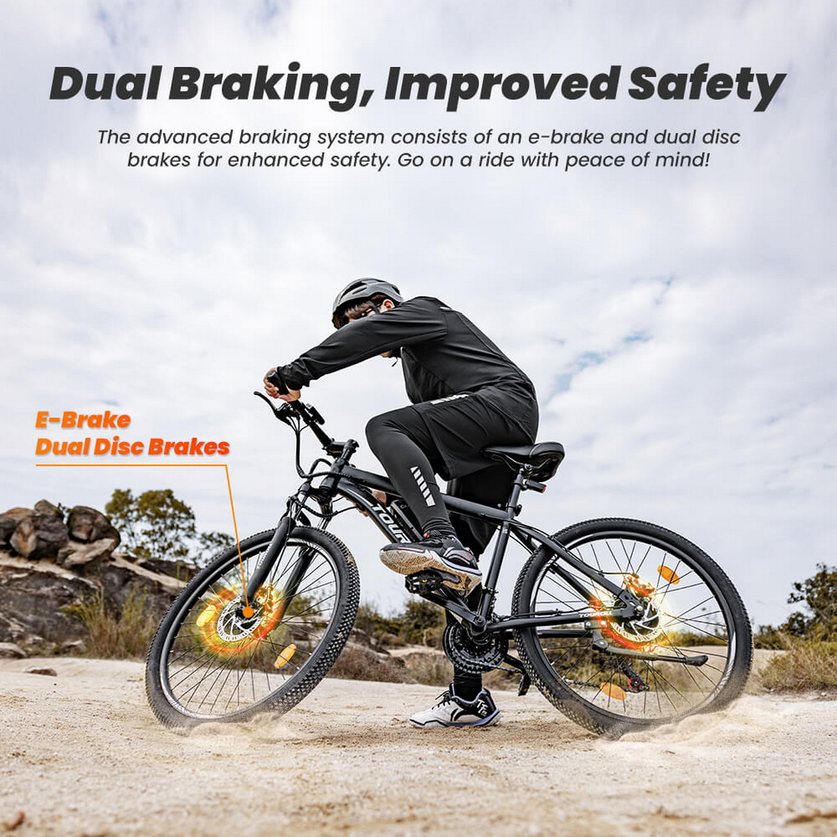 Osoba jadąca czarnym rowerem z podwójnymi hamulcami tarczowymi na piaszczystej drodze, zachmurzone niebo.