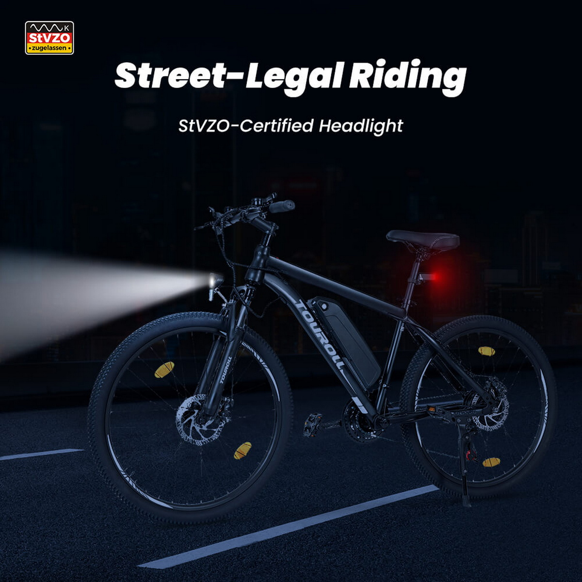 Czarny rower elektryczny na ciemnej drodze, z jasnym reflektorem i czerwonym światłem tylnym.