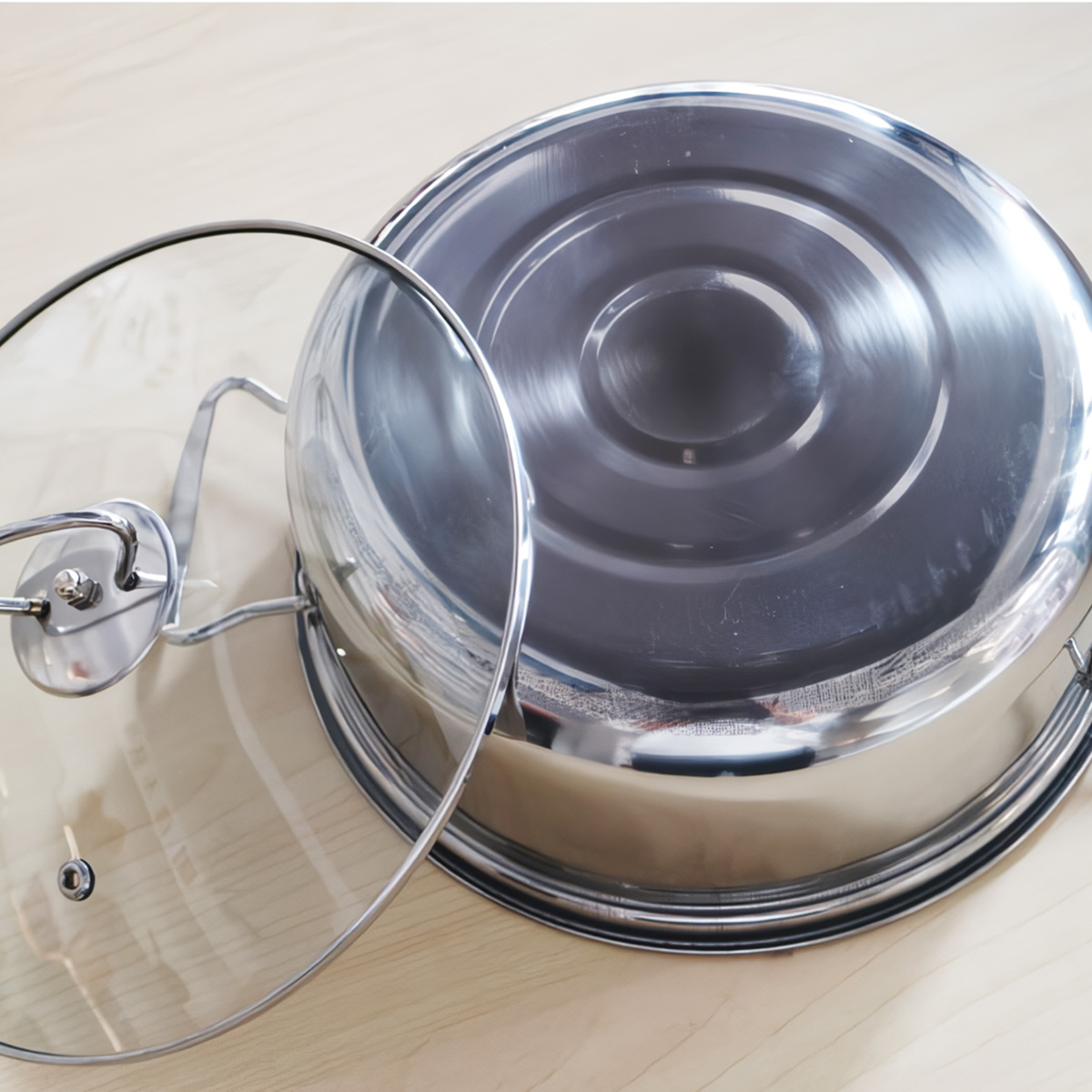 Olla de acero inoxidable con tapa de cristal, la tapa está quitada y apoyada en la olla.