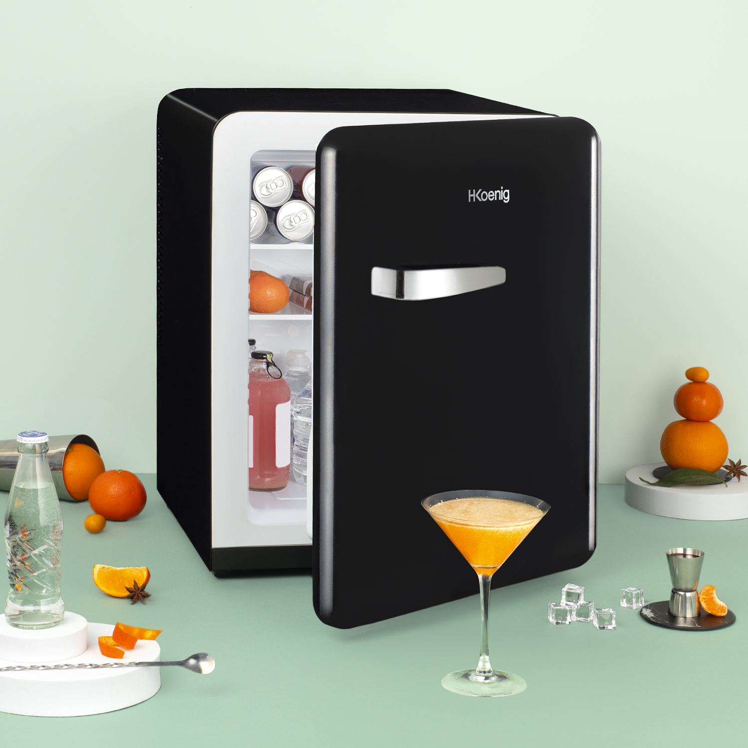Mini frigo nero, porta aperta, con bevande, bicchiere da martini, arance.