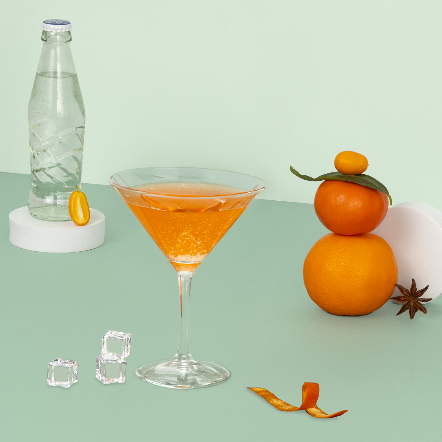 Cocktail all'arancia in un bicchiere da Martini con cubetti di ghiaccio e una bottiglia d'acqua sullo sfondo.