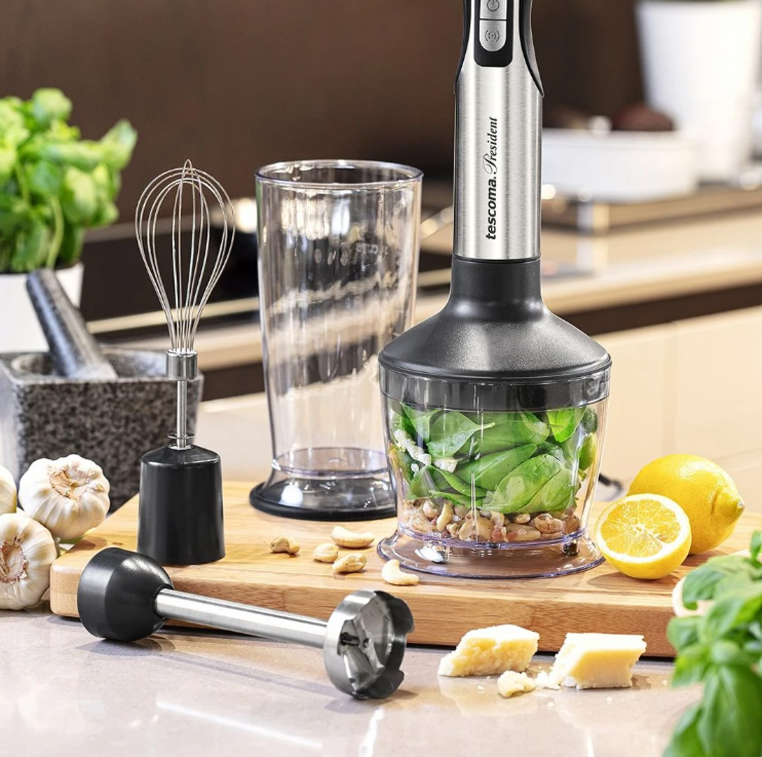 Stabmixer mit Zutaten: Basilikum, Nüsse, Zitrone und Parmesan auf einem Holzbrett.