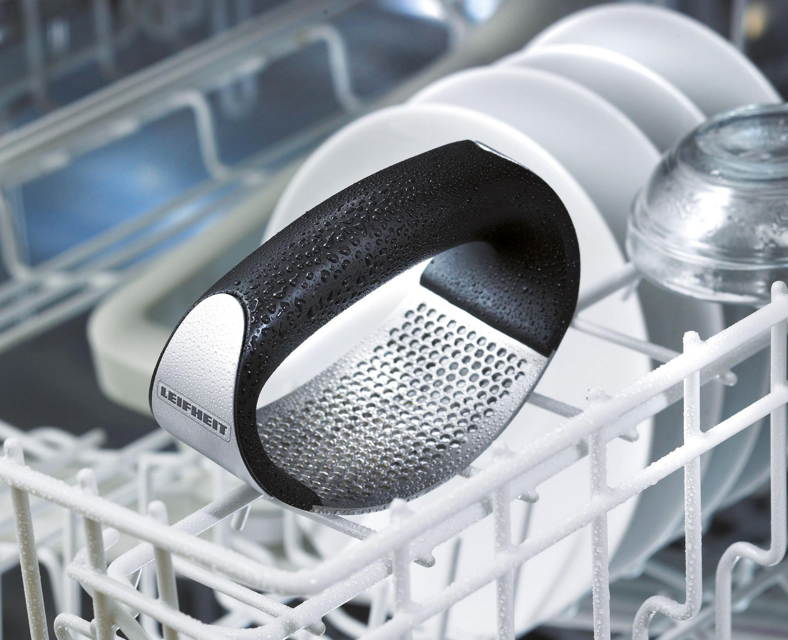 Srebrna i czarna tarka w zmywarce. Białe naczynia po prawej. Zbliżenie.