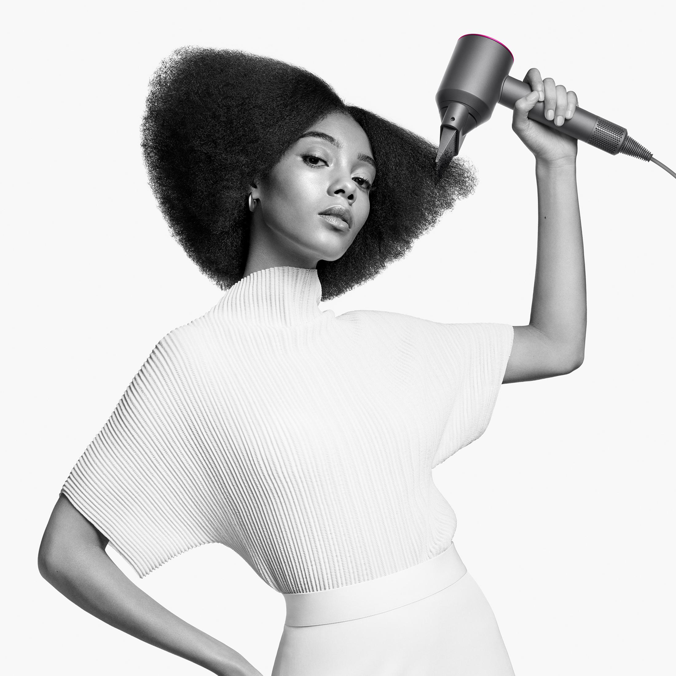 Kobieta trzymająca suszarkę Dyson, pozująca na białym tle.