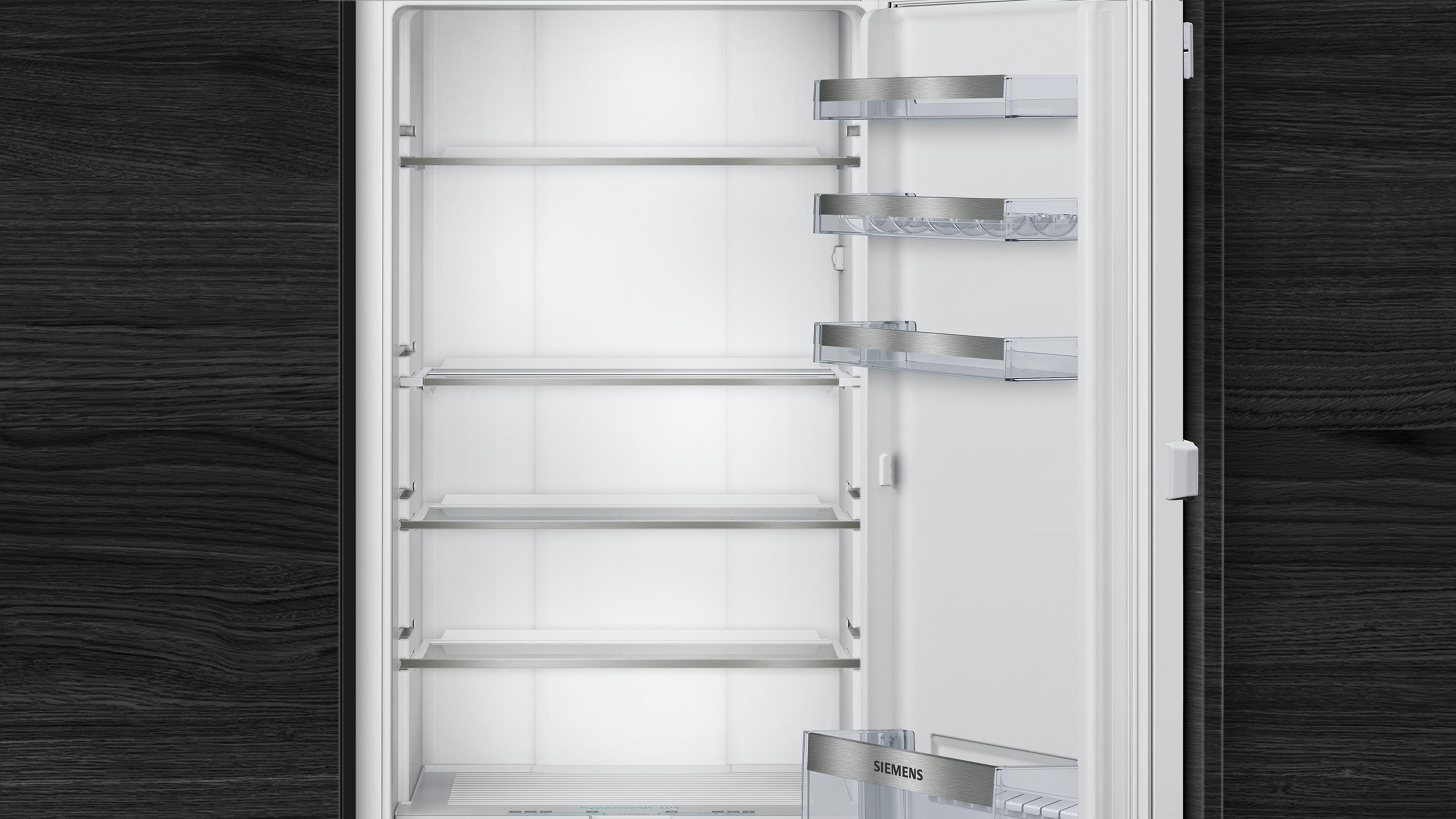 Leeg wit koelkastinterieur met planken, tegen een donkere achtergrond met houtnerf.