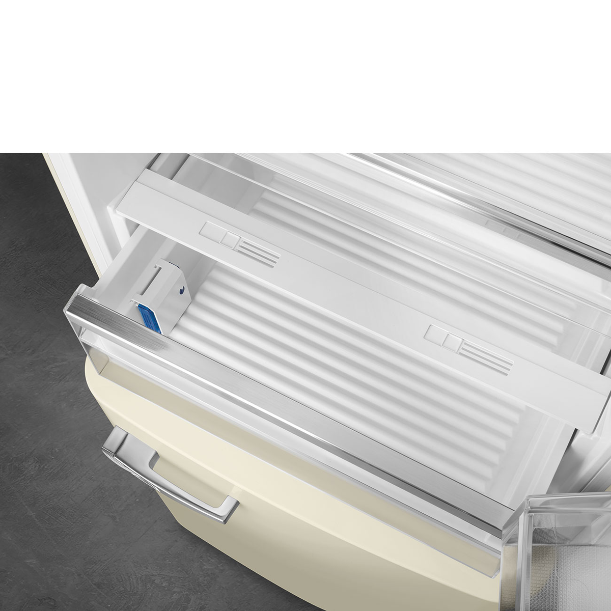 Primer plano del interior del cajón del refrigerador, de color crema claro y con manija de metal.