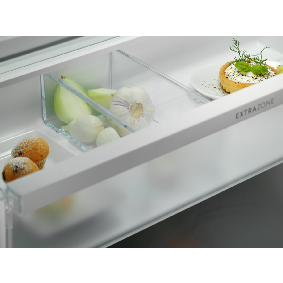 Primo piano di un cassetto del frigorifero contenente cipolle, aglio e pasticcini con il testo EXTRAZONE visibile.