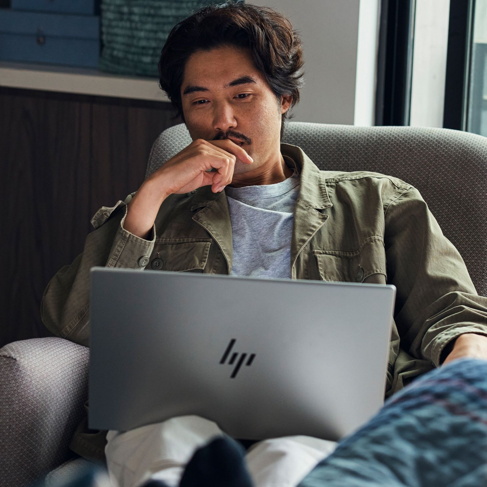 Mężczyzna w pokoju używający srebrnego laptopa HP na kolanach.