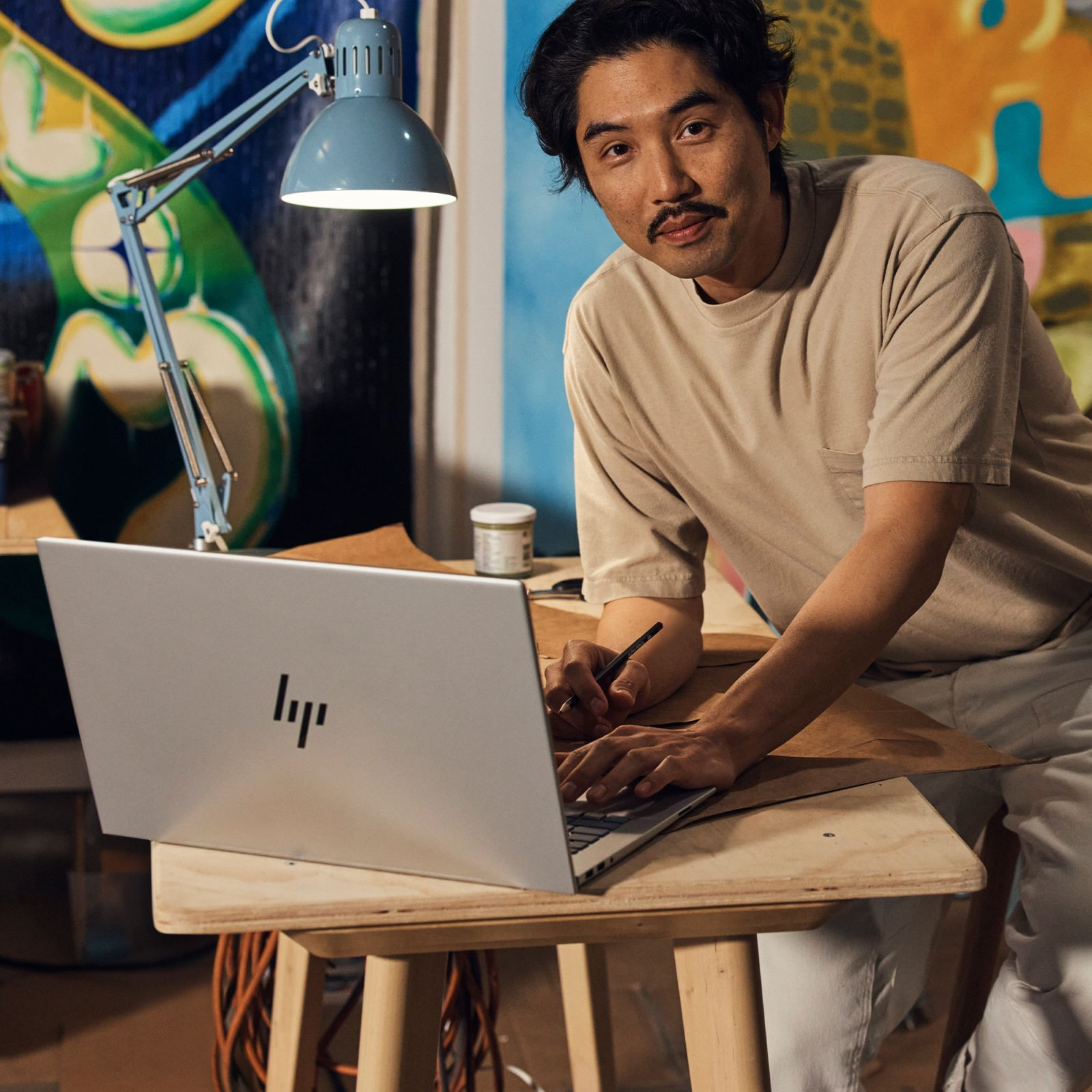 Mężczyzna pracuje na srebrnym laptopie przy drewnianym stole. Niebieska lampa po lewej stronie.