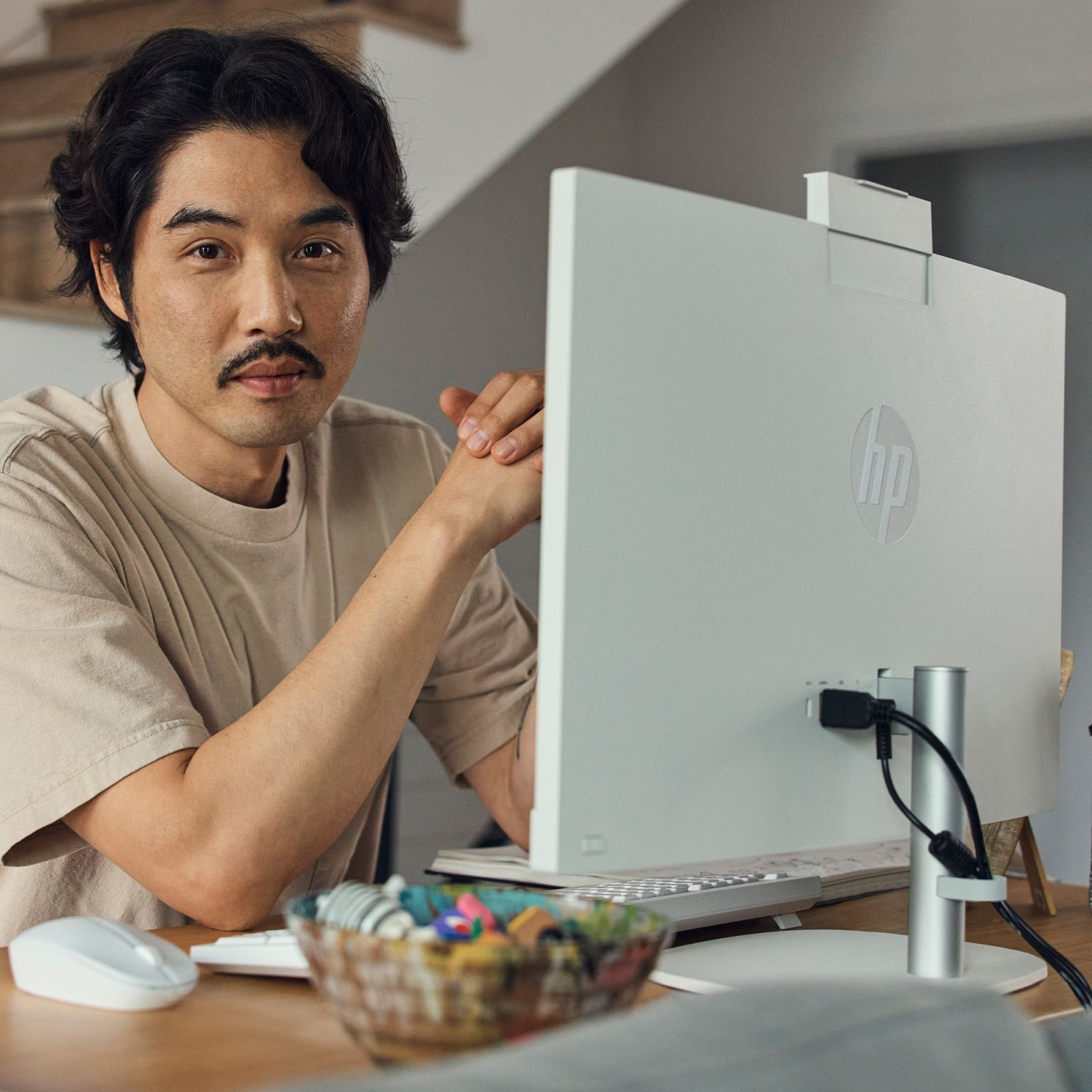 Mężczyzna z wąsami siedzi przy biurku z białym monitorem i myszką komputerową.