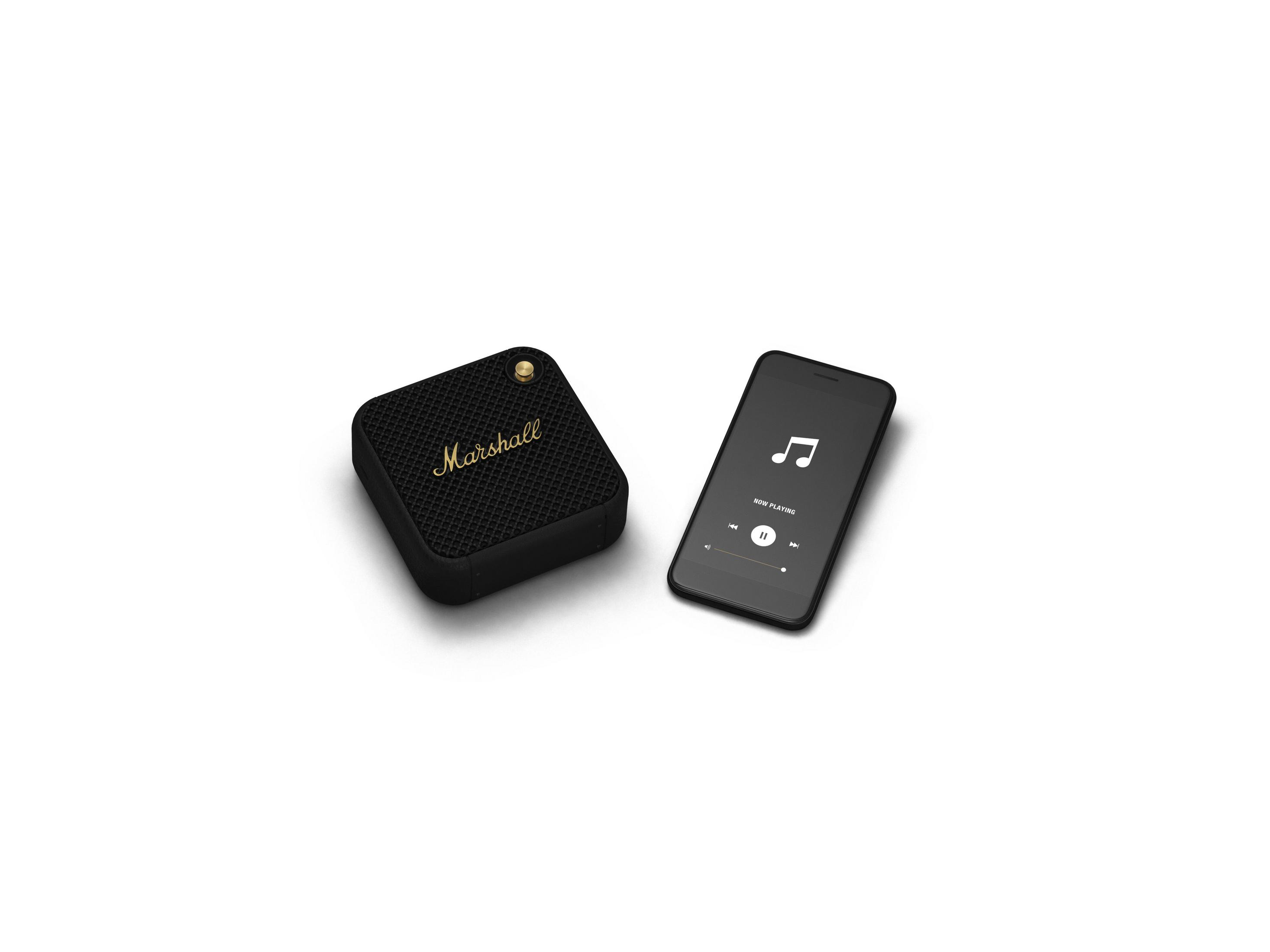 Altoparlante Marshall nero e uno smartphone che riproduce musica. Entrambi sono su una superficie bianca. Logo Marshall visibile.