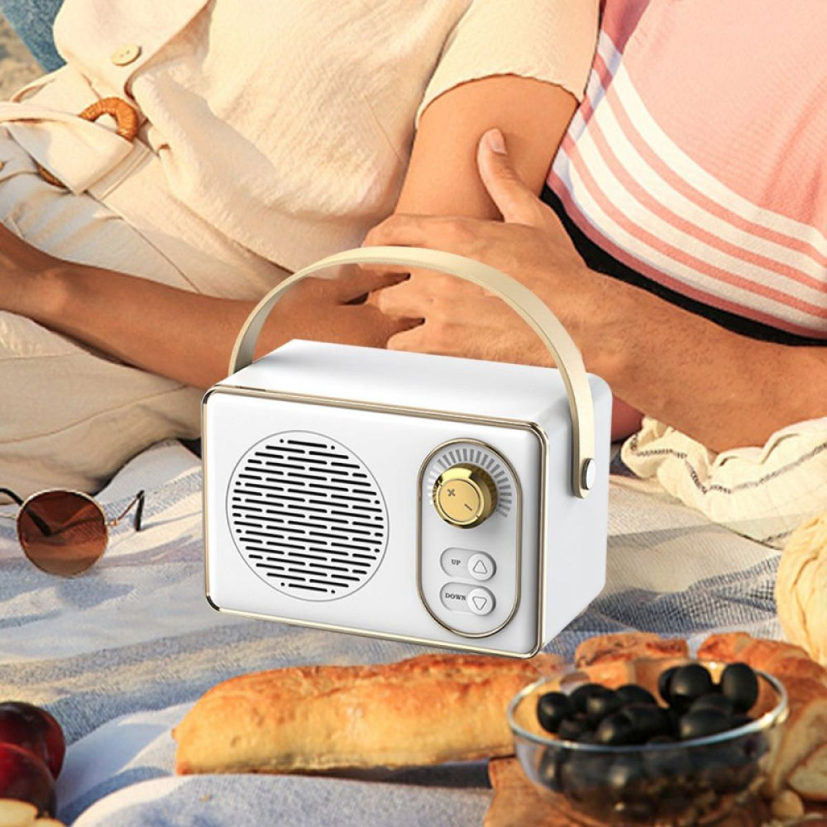 Weißer Lautsprecher im Retro-Stil mit Griff. Personen im Hintergrund sitzen, Picknick-Einstellung.