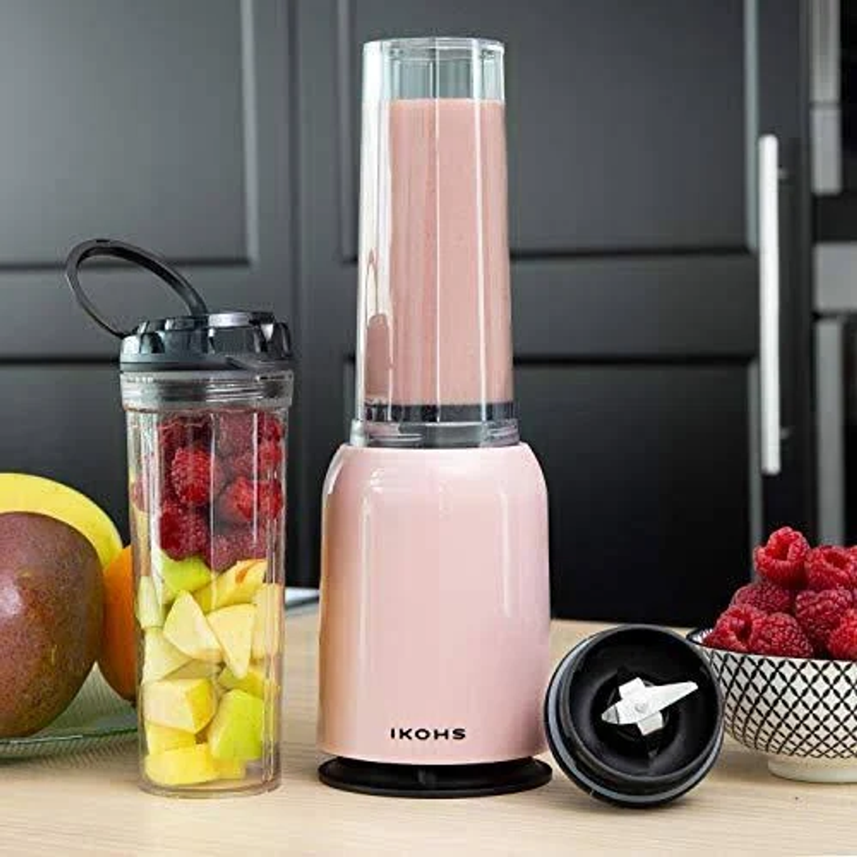 Batidora rosa con batido en vaso alto, ingredientes de frutas: frambuesas, mango y manzana.