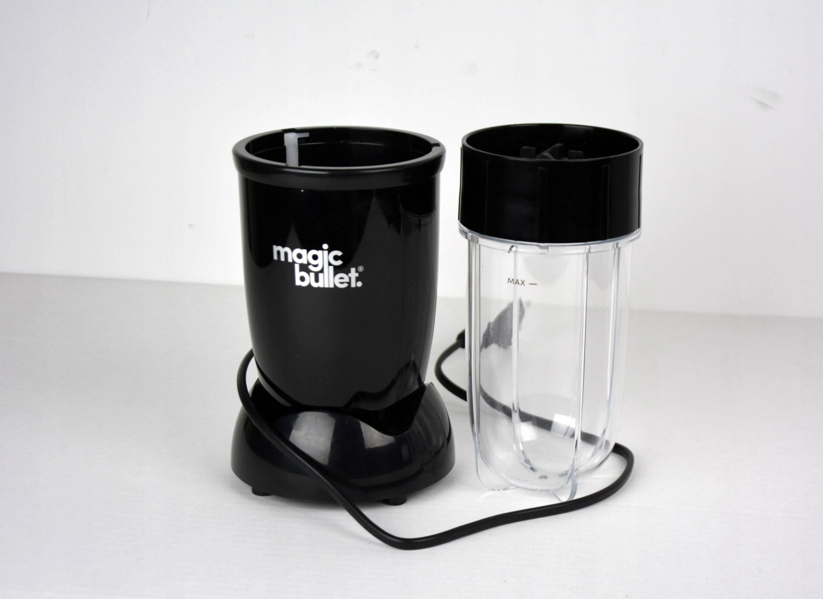 Base del frullatore Magic Bullet nera e tazza di miscelazione trasparente con coperchio nero su superficie bianca.