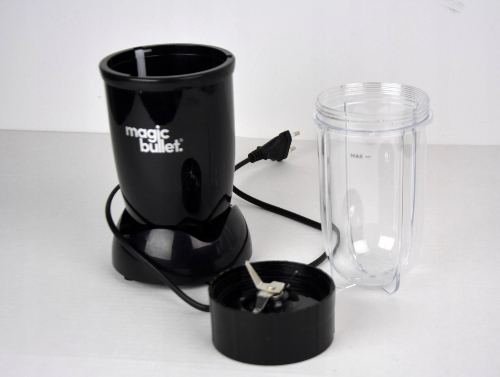Frullatore nero Magic Bullet con lama staccata e contenitore trasparente. Cavo di alimentazione visibile.