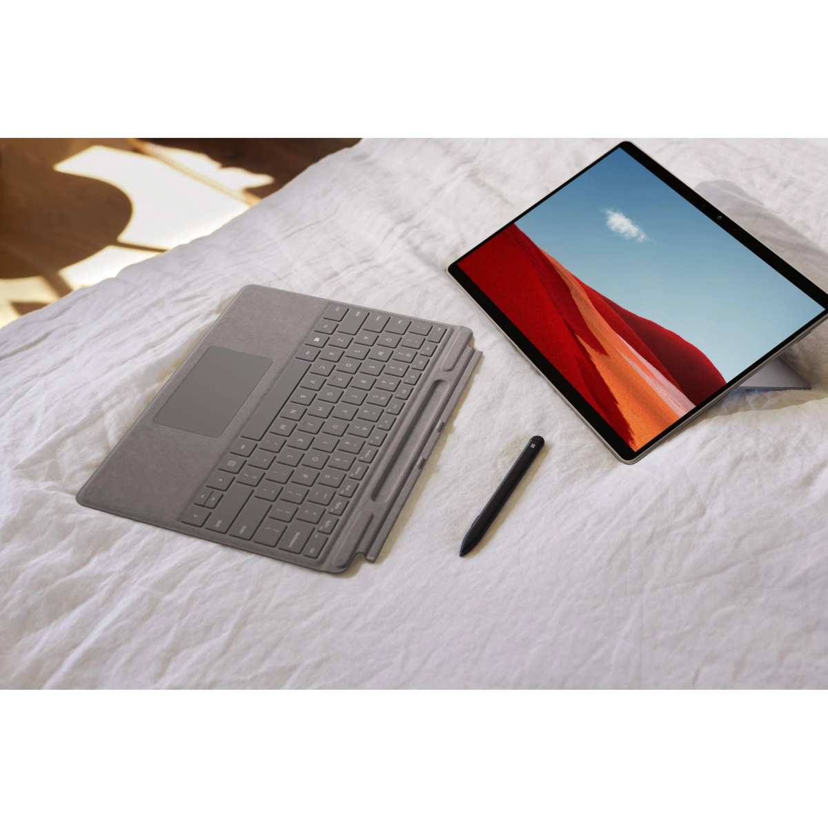 Ein Laptop mit einem Bildschirm, der ein abstraktes Design zeigt, eine Tastatur und ein Stift auf einem weißen Bettlaken.
