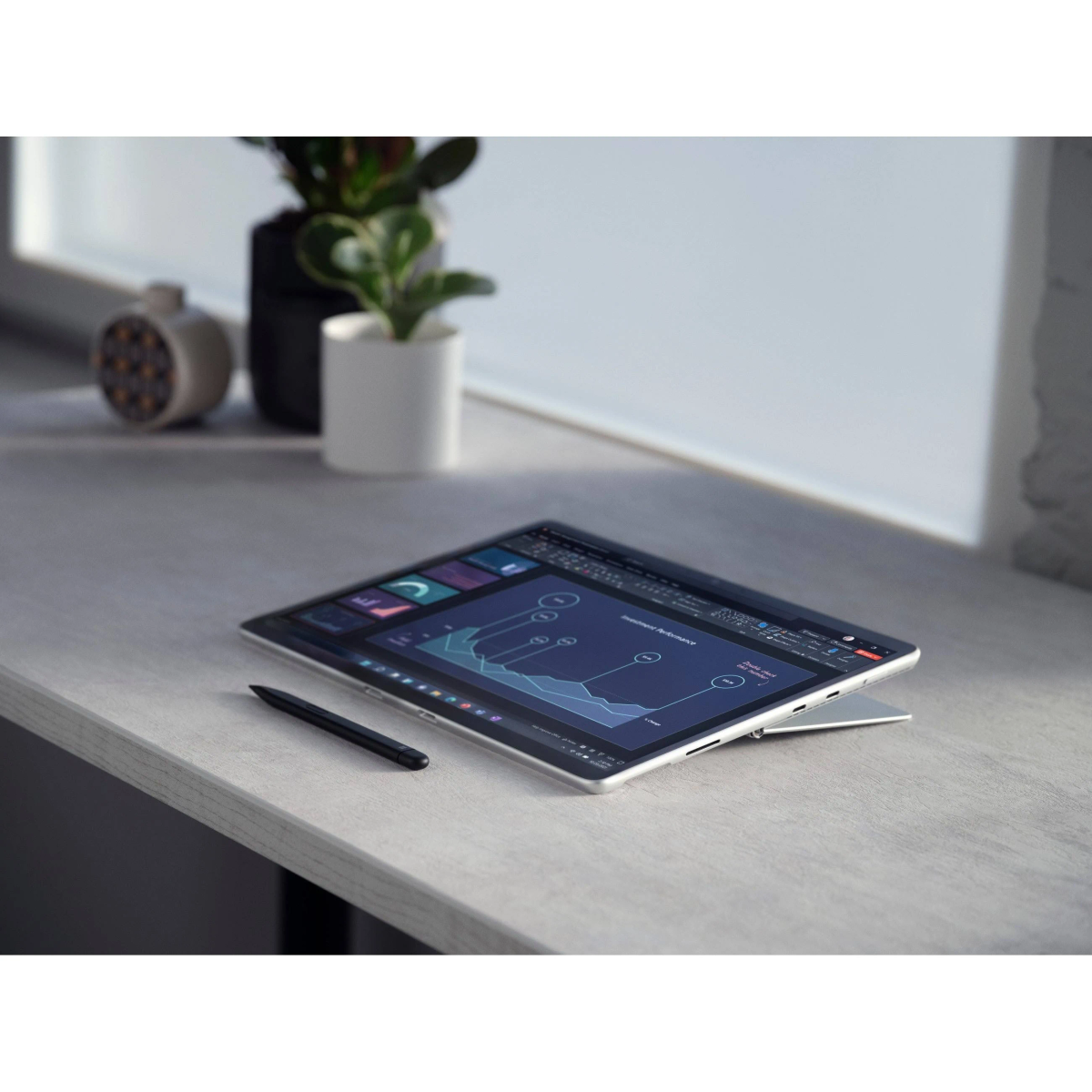 Tablet mit Diagramm, Stift auf hellgrauem Schreibtisch, in der Nähe von Fenster und Pflanzen.