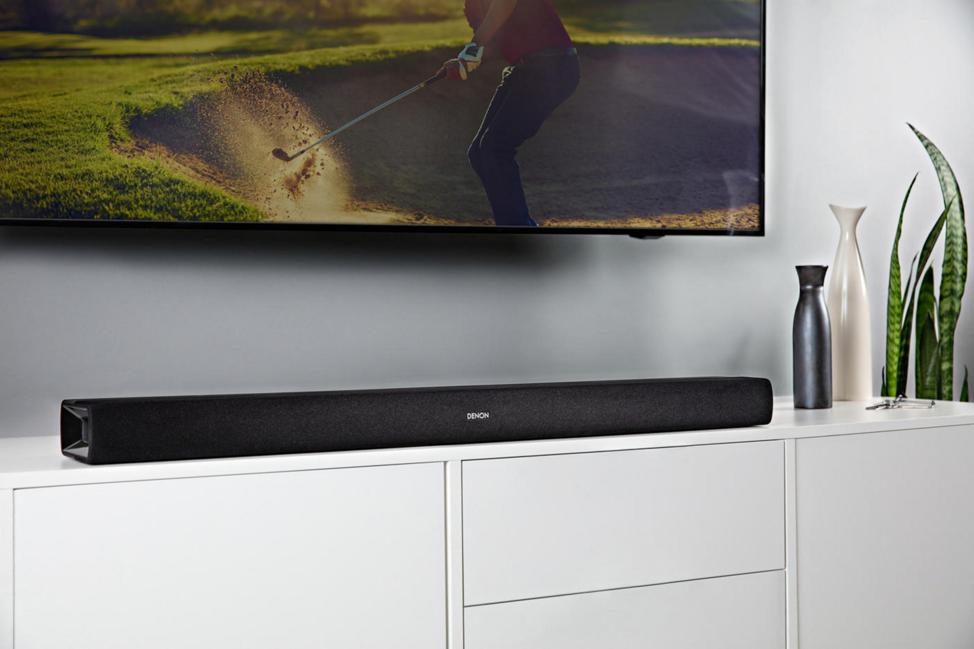 Schwarze Soundbar unter einem Fernseher, weißer Schrank mit Vasen und Golfplatz-Szene im Fernseher.
