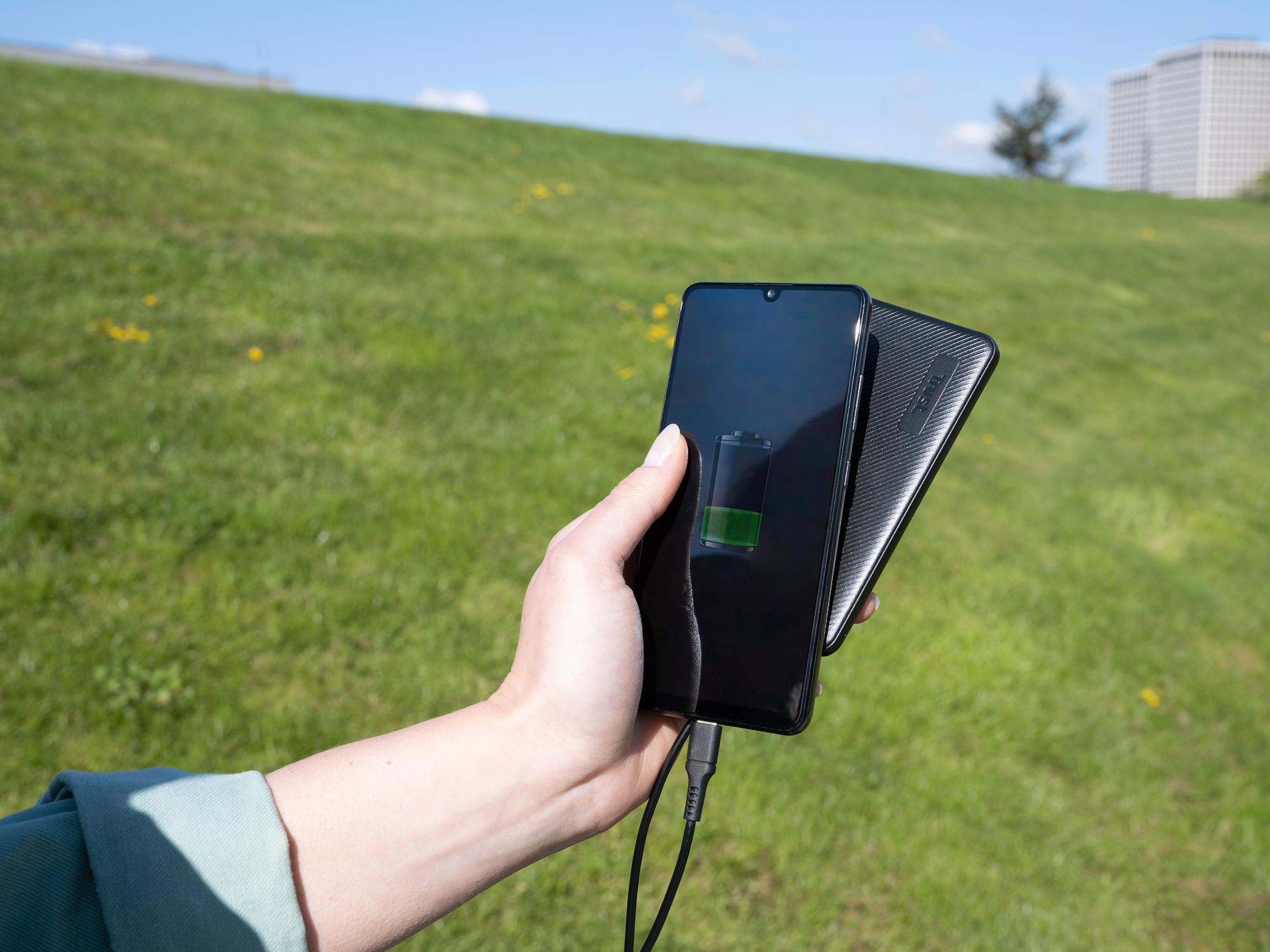 Hand die een zwarte smartphone vasthoudt die draadloos oplaadt naast een oplaadpad, groen veld.