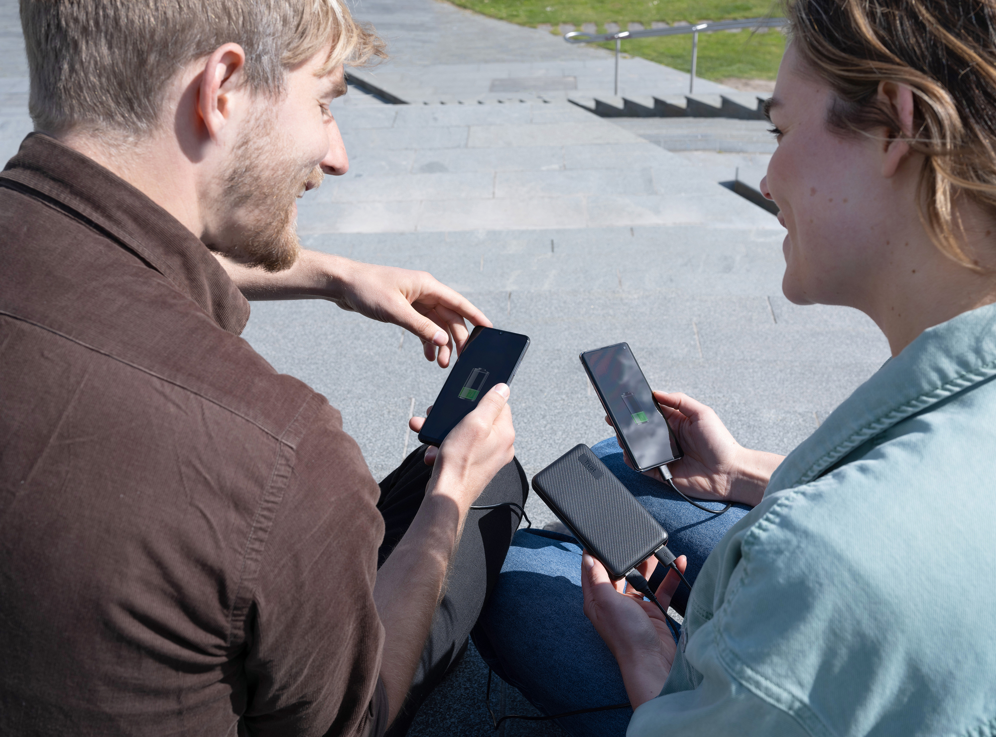 Twee mensen delen stroom van een powerbank om telefoons op te laden.
