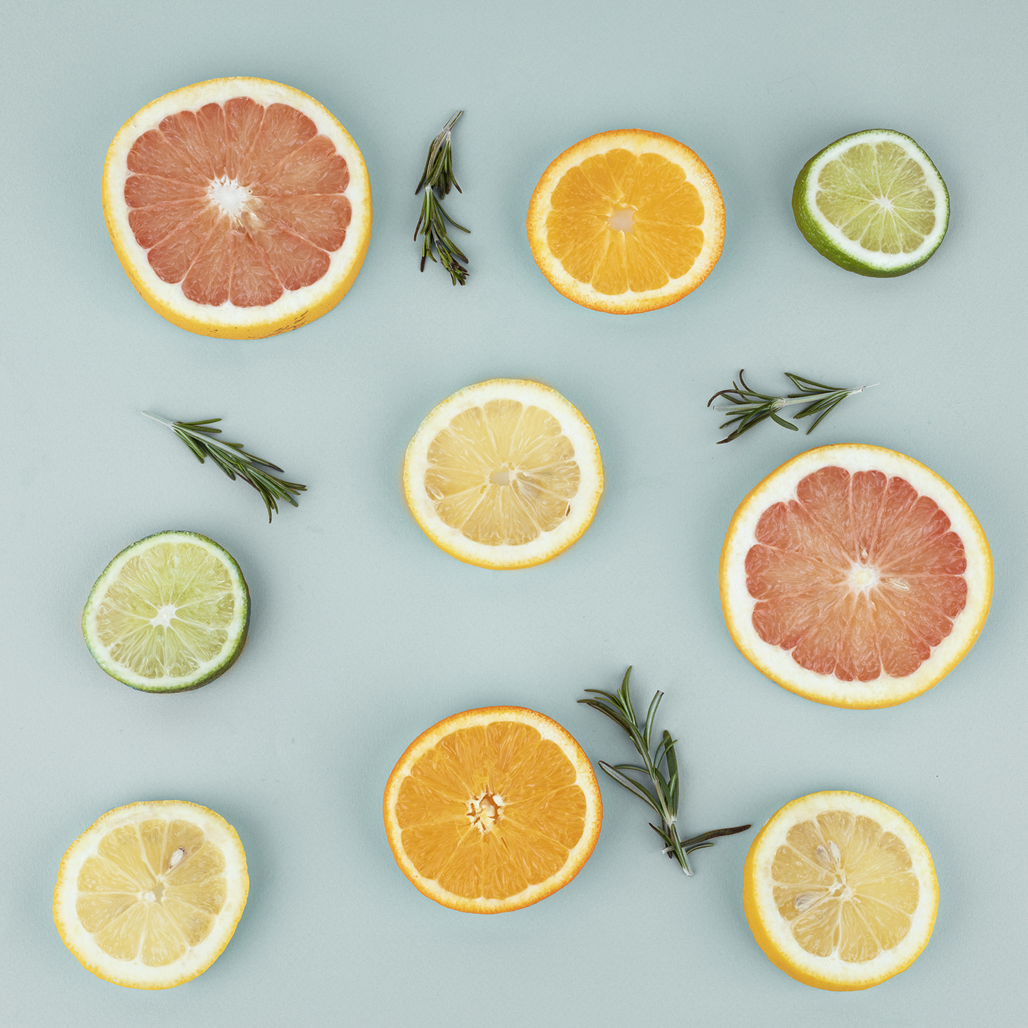 Krojone owoce cytrusowe i gałązki rozmarynu na jasnoniebieskiej powierzchni.