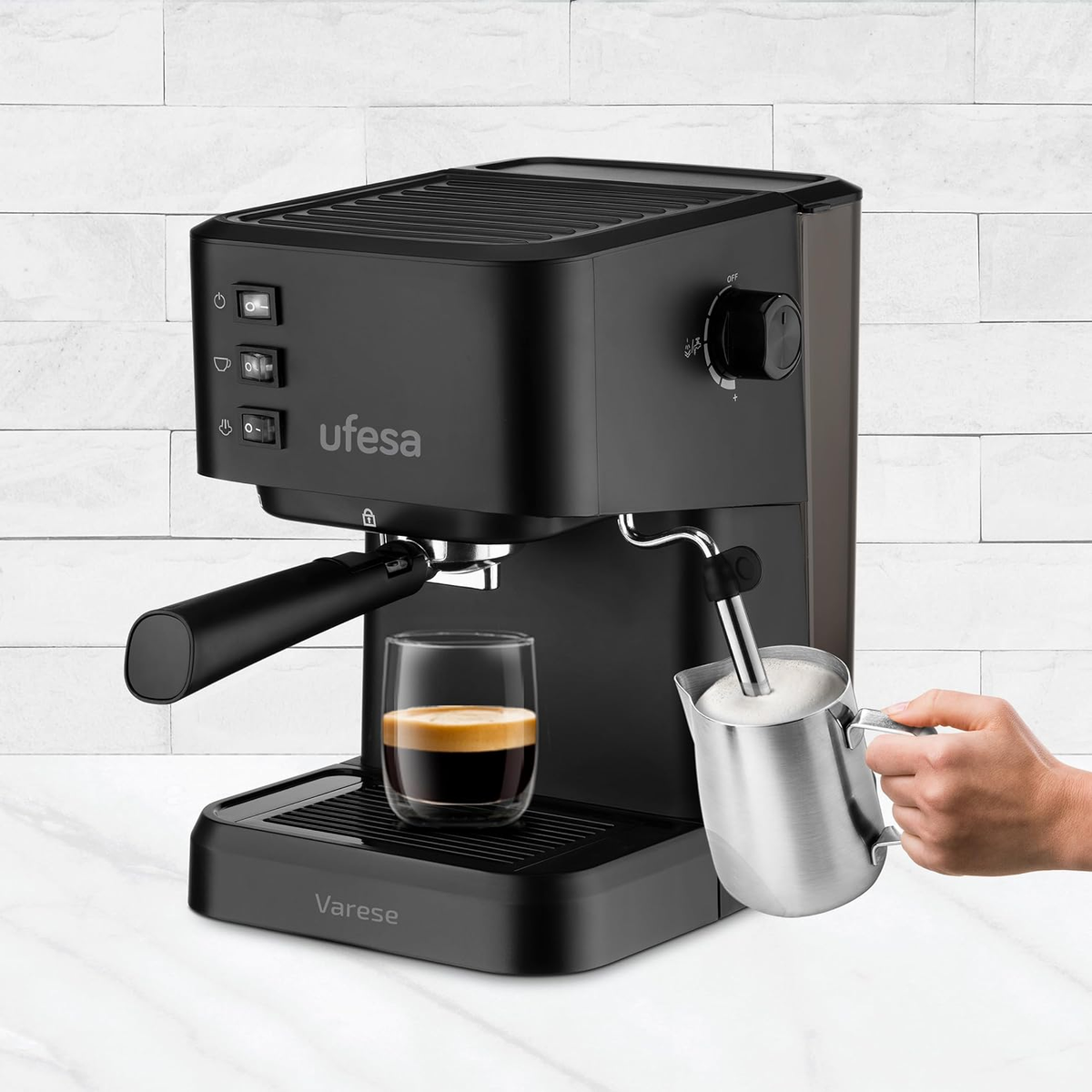 Máquina de espresso negra con vaso de café y mano espumando leche.