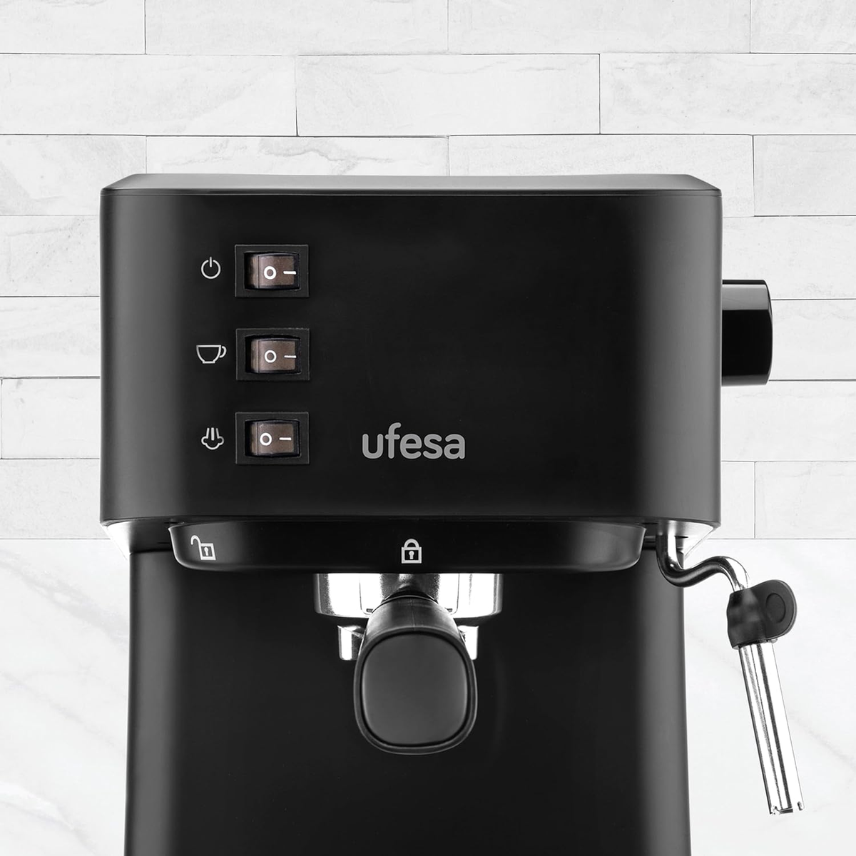 Una cafetera espresso Ufesa negra. Tiene botones de encendido, café y vapor. Fondo de baldosas blancas.