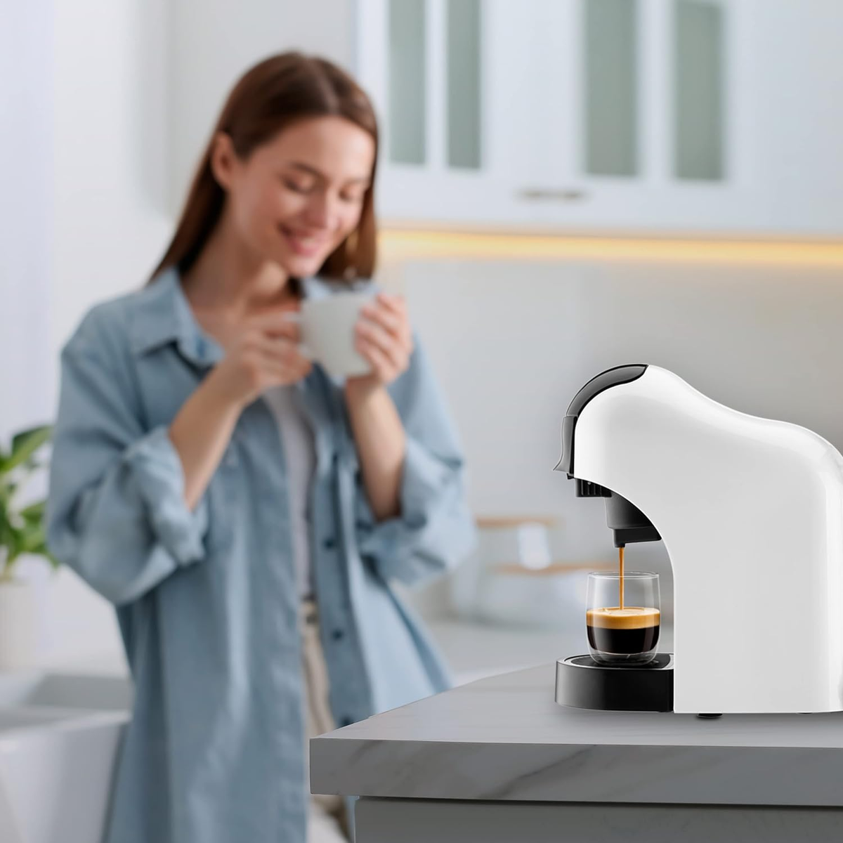 Donna che tiene una tazza di caffè, e accanto a lei una macchina da caffè bianca.