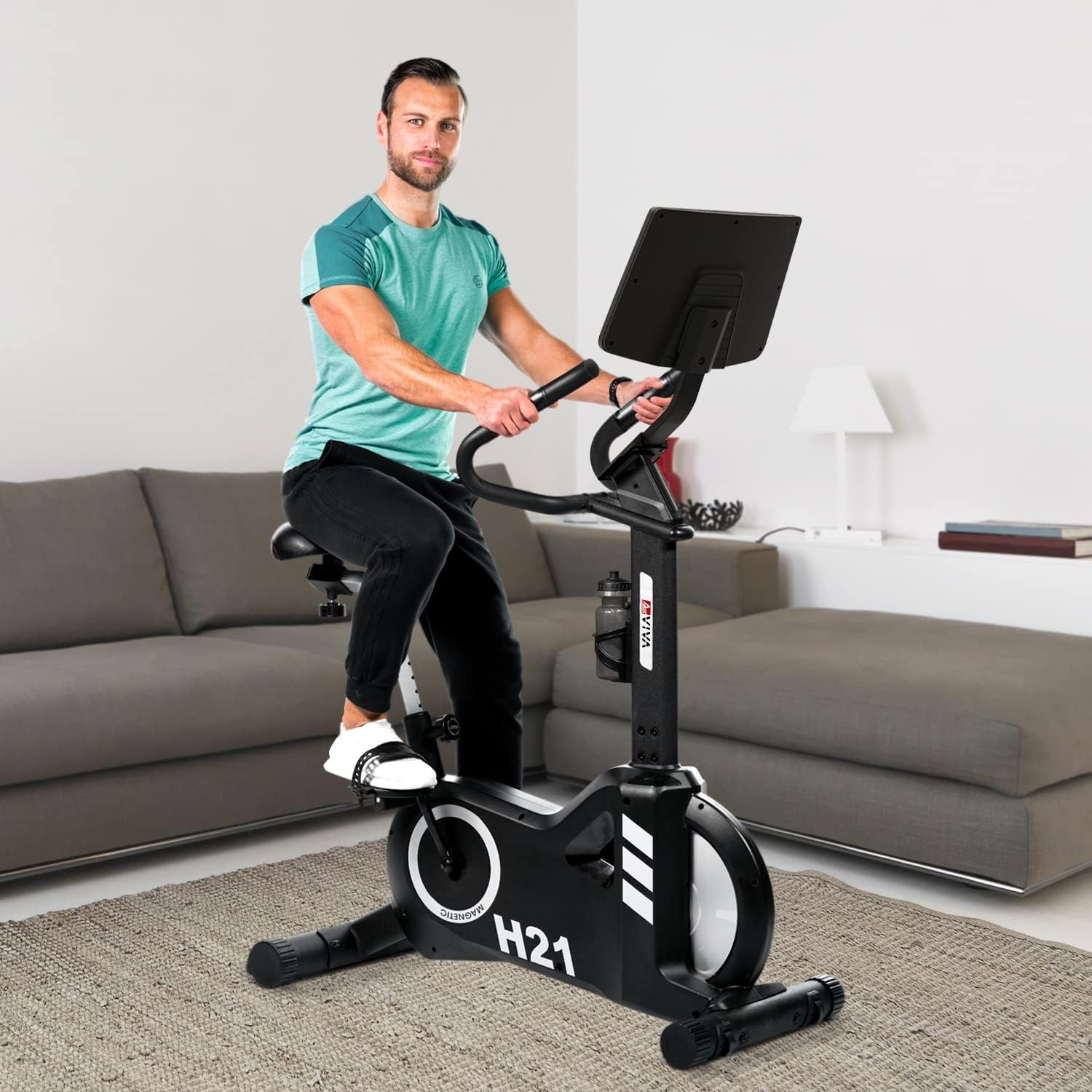 Mann auf einem schwarzen Heimtrainer. Er trägt ein türkisfarbenes Hemd und schwarze Hosen und schaut in die Kamera.